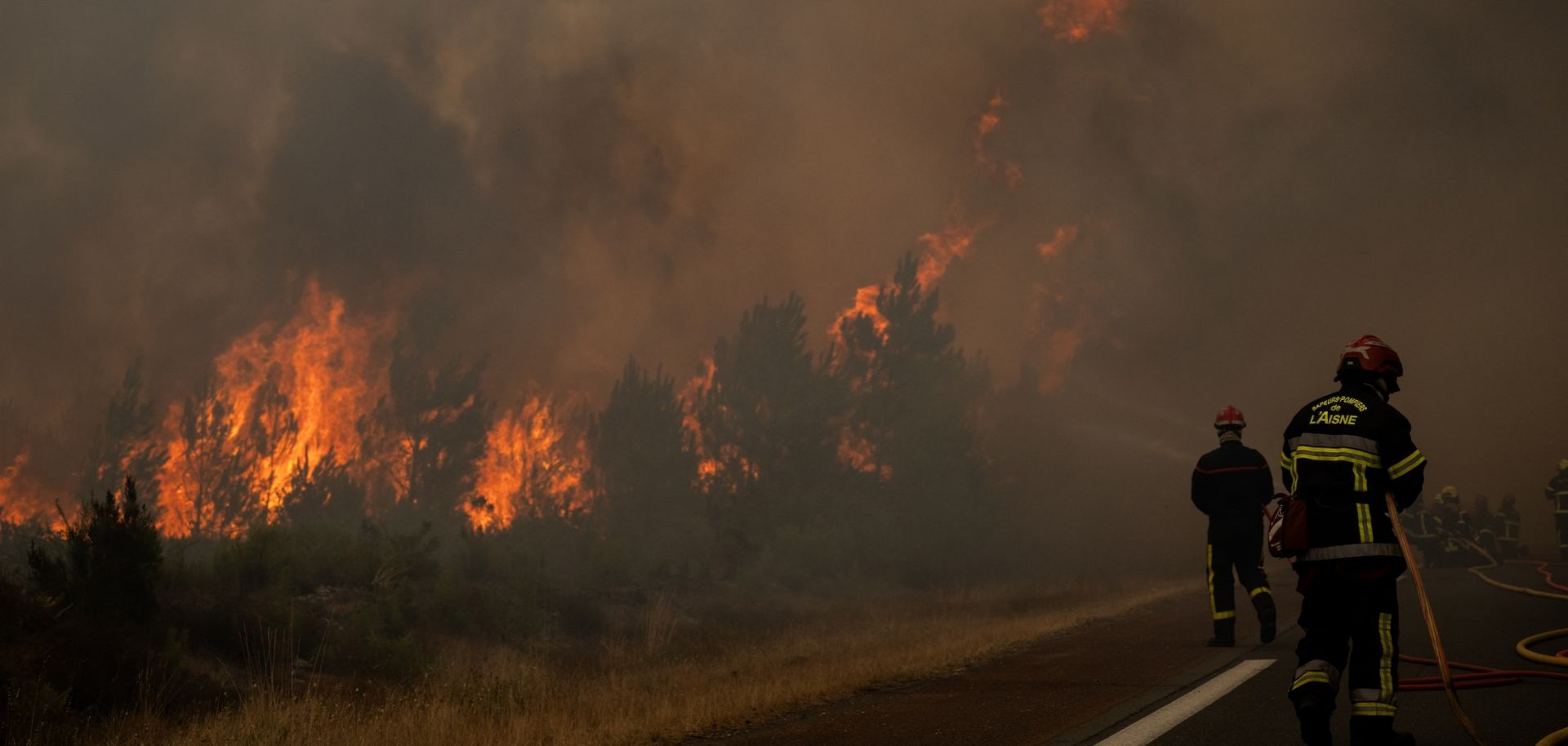 Firefighters spray water along the edge of a forest during a wildfire in southwestern France on July 25, 2026. 