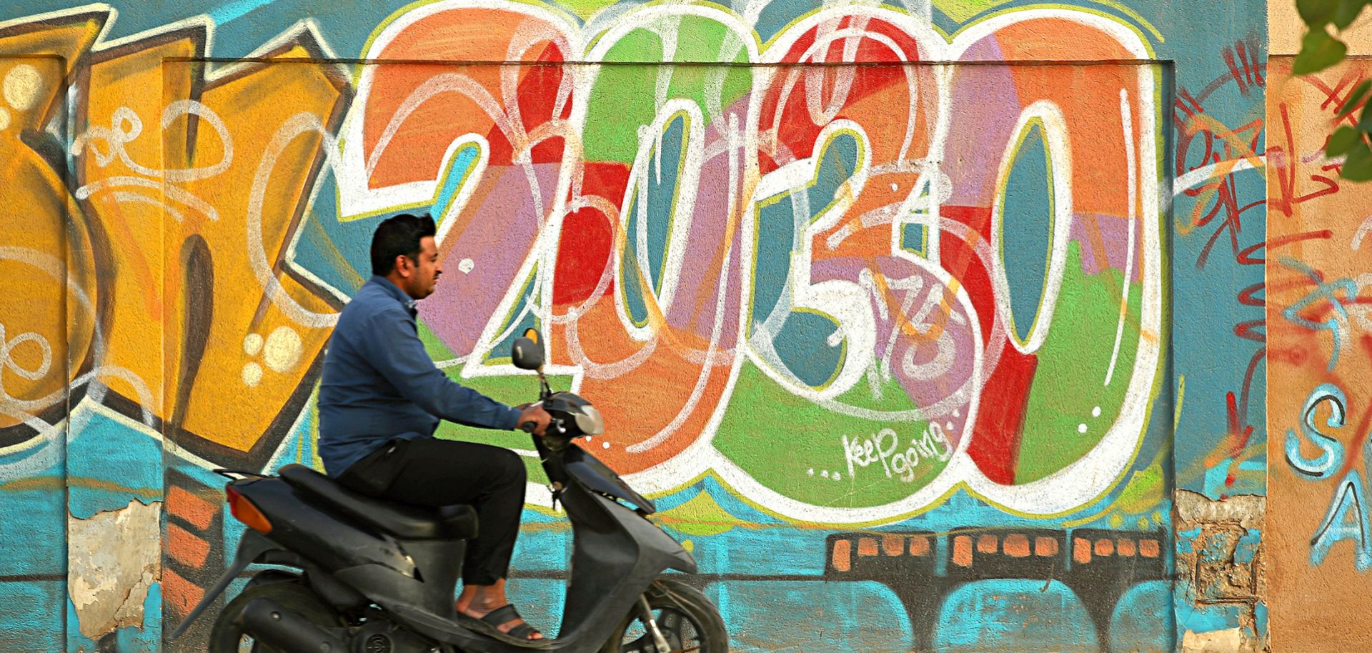 This photo shows a scooter rider passing graffiti alluding to the Saudi Vision 2030 modernization program
