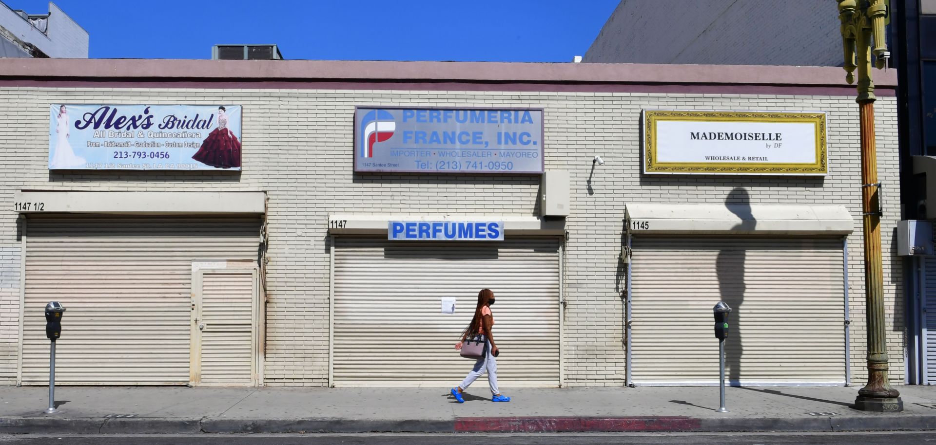 A woman walks past closed shopfronts in what would be a normally busy fashion district in Los Angeles, California, on May 4, 2020. 