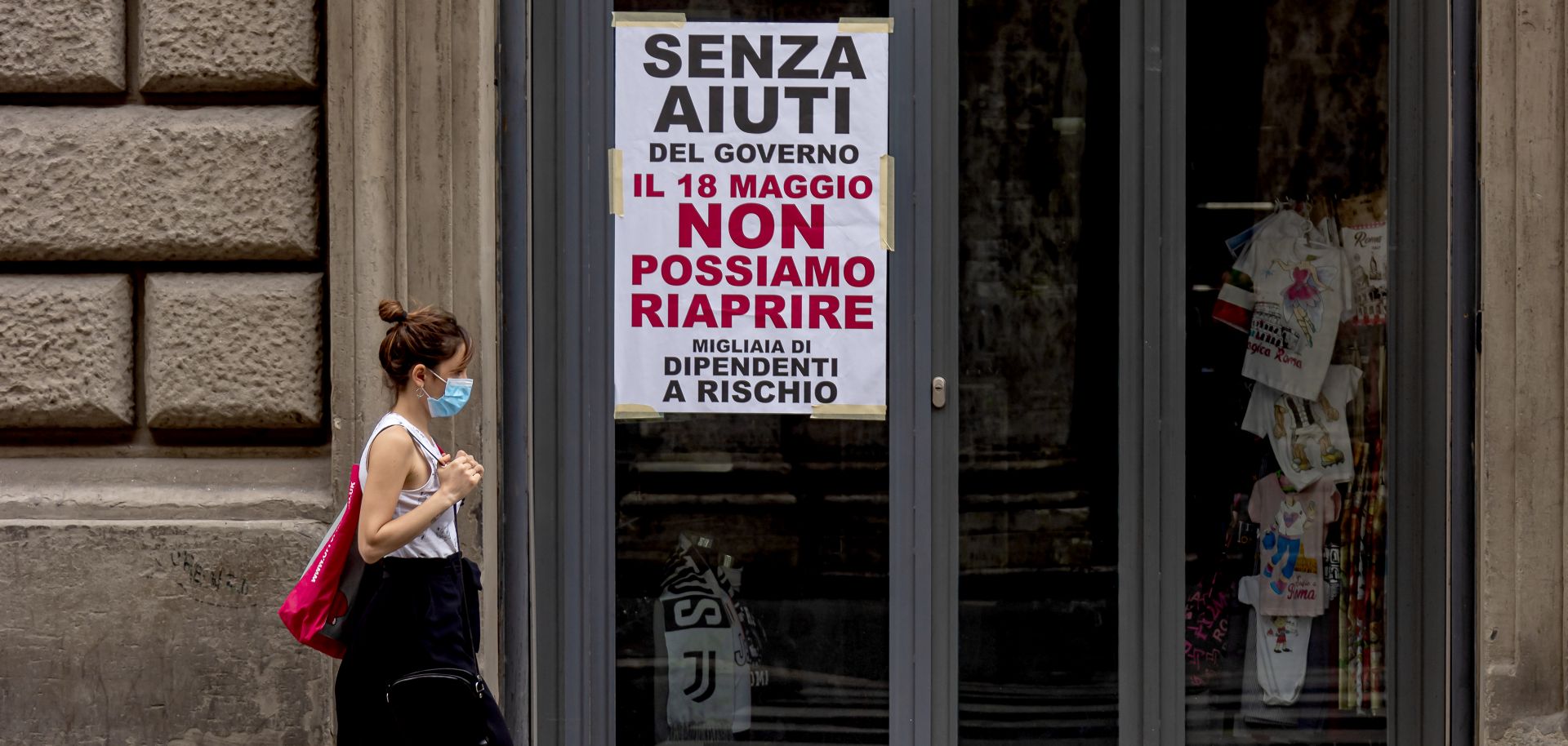 A woman wearing a face mask walks past a closed shop in Rome, Italy, on May 18, 2020. The sign on the store window reads "Without government aid, we cannot reopen on May 18. Thousands of employees at risk." 