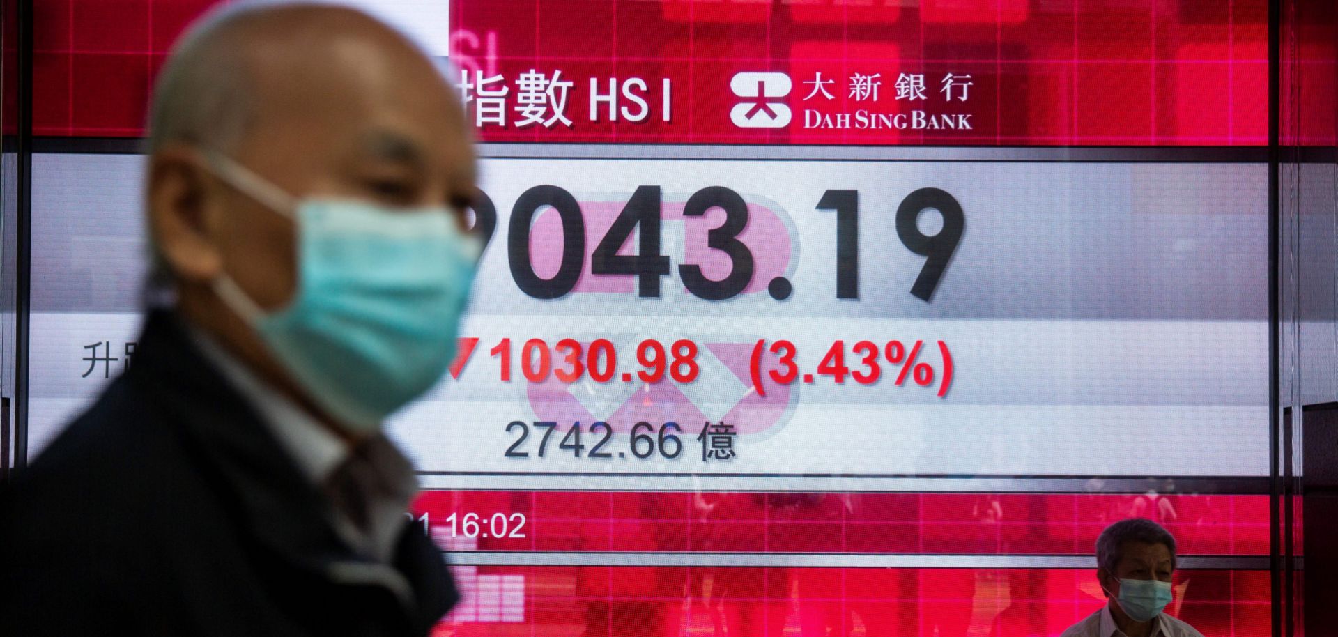 People walk past an electronic display showing Hong Kong’s Hang Seng Index in the city’s central district on Feb. 26, 2021. 