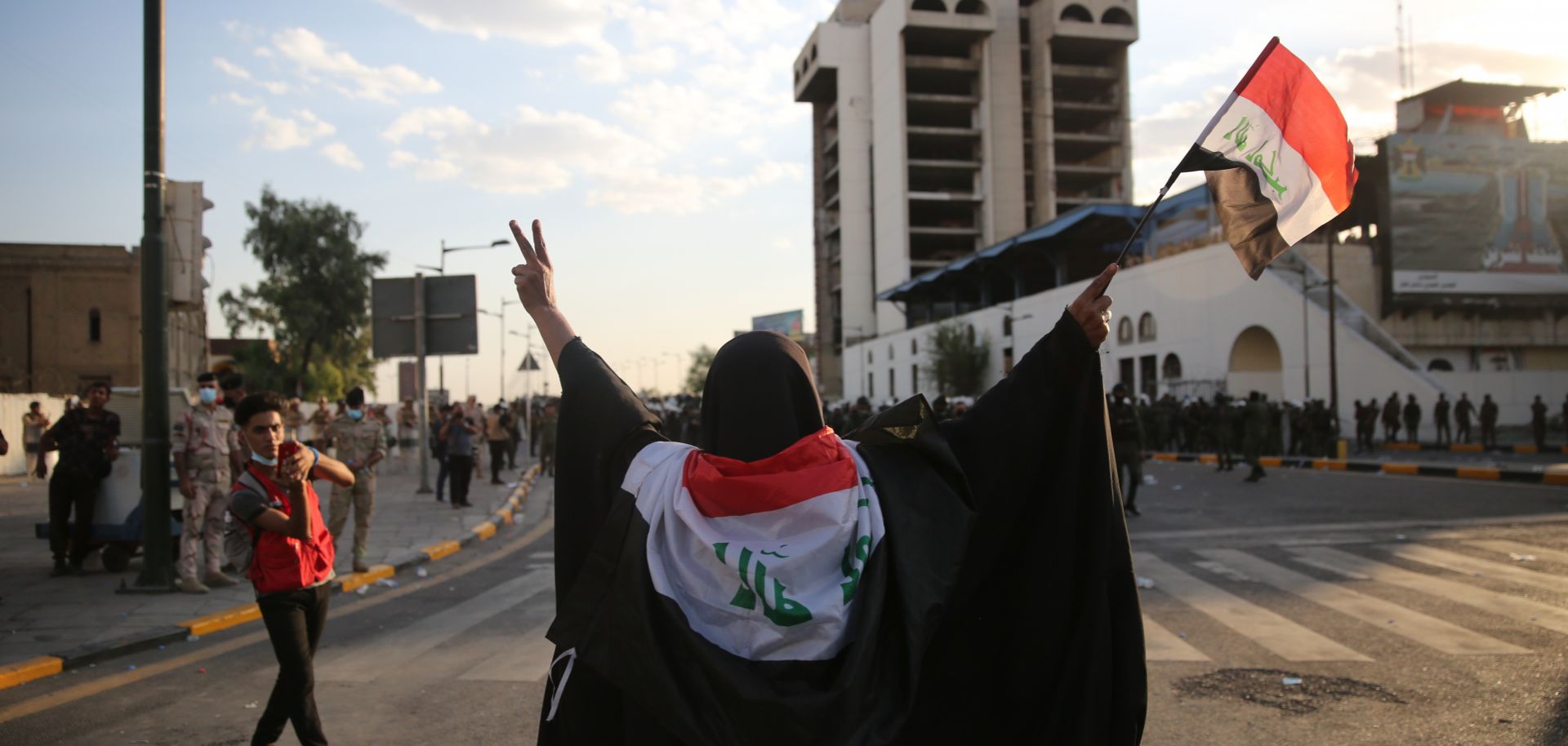 A woman waves an Iraqi flag as riot police charge toward protesters in Baghdad on May 25, 2021.
