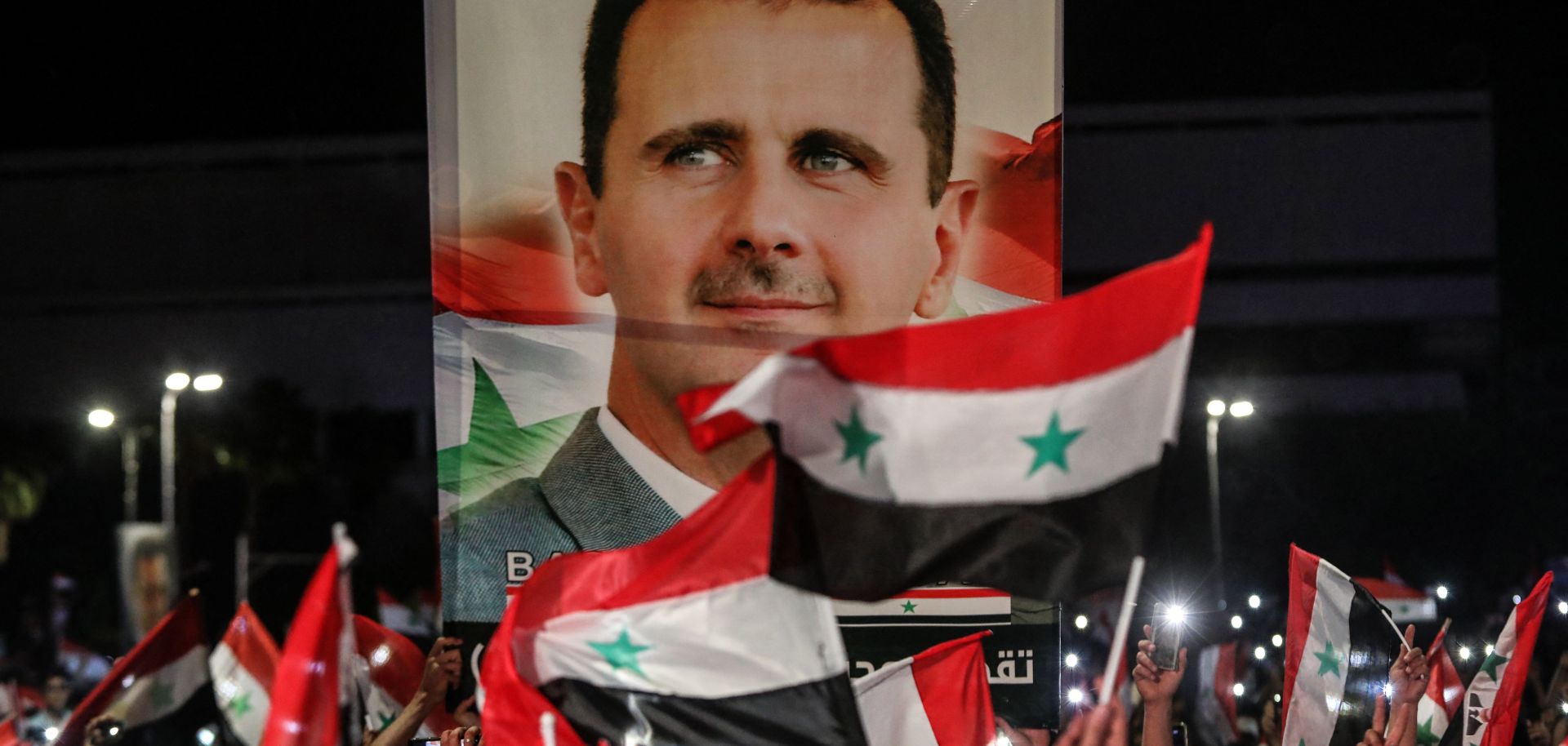 Syrians wave national flags and carry a large portrait of President Bashar al Assad in the streets of Damascus on May 27, 2021.