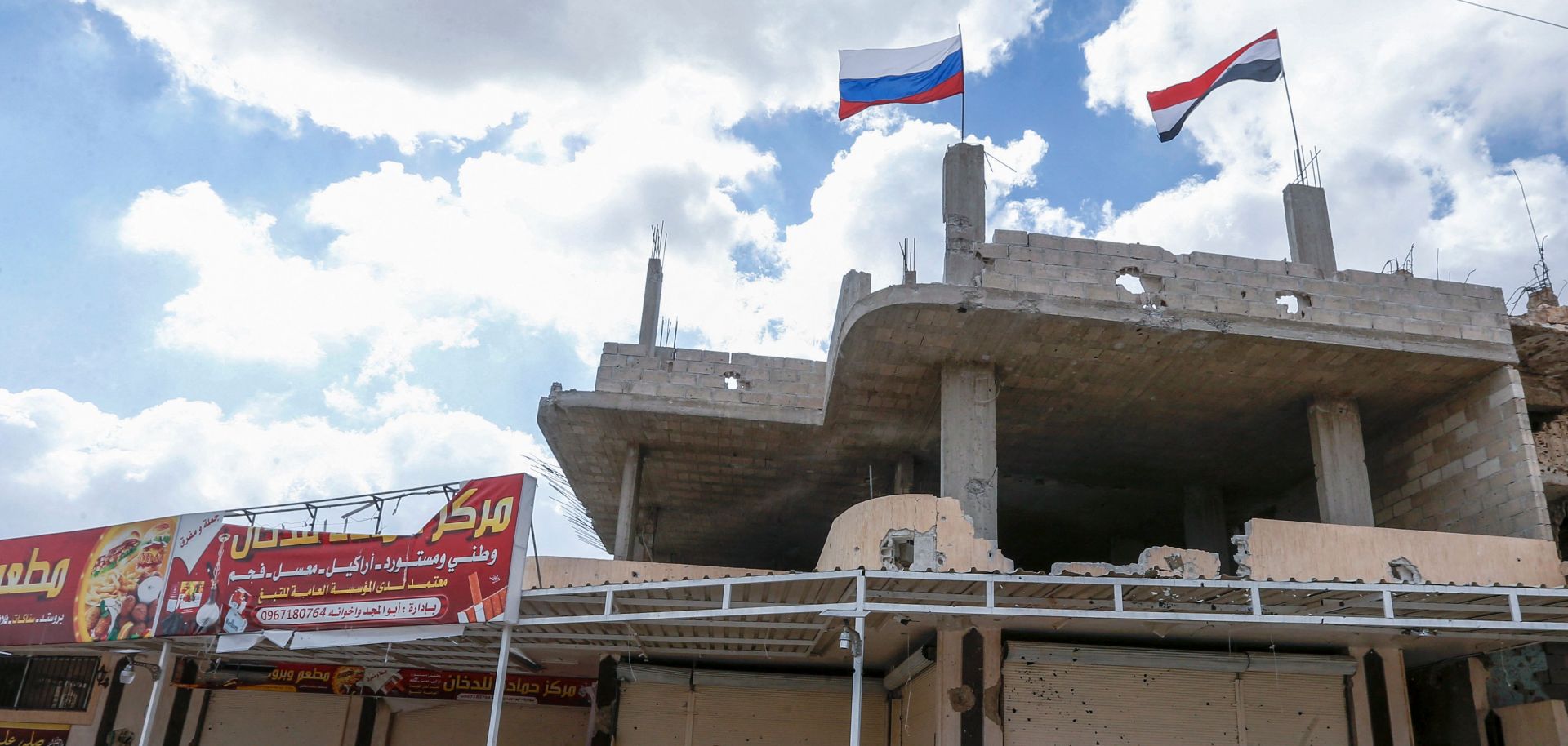Russian and Syrian flags wave above a damaged building in Syria's southern city of Daraa on Sept. 12, 2021.
