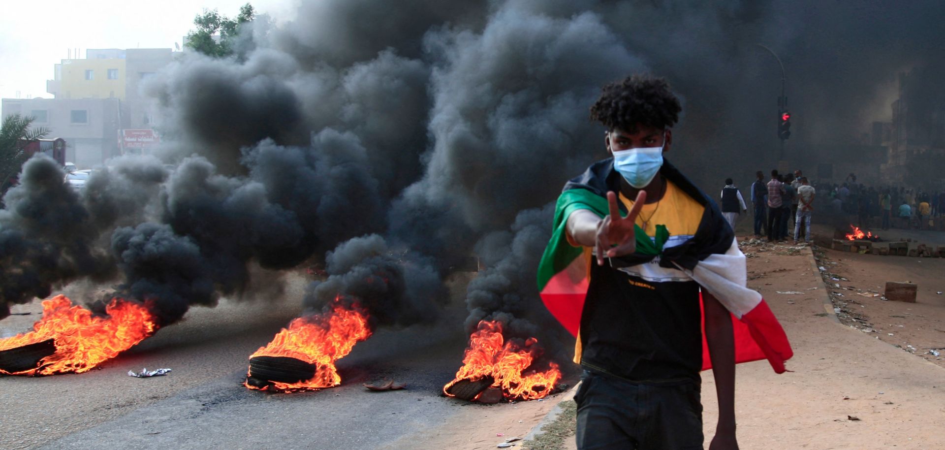 A protester draped with Sudan’s national flag stands in front of burning tires during a demonstration in Khartoum on Oct. 25, 2021. 