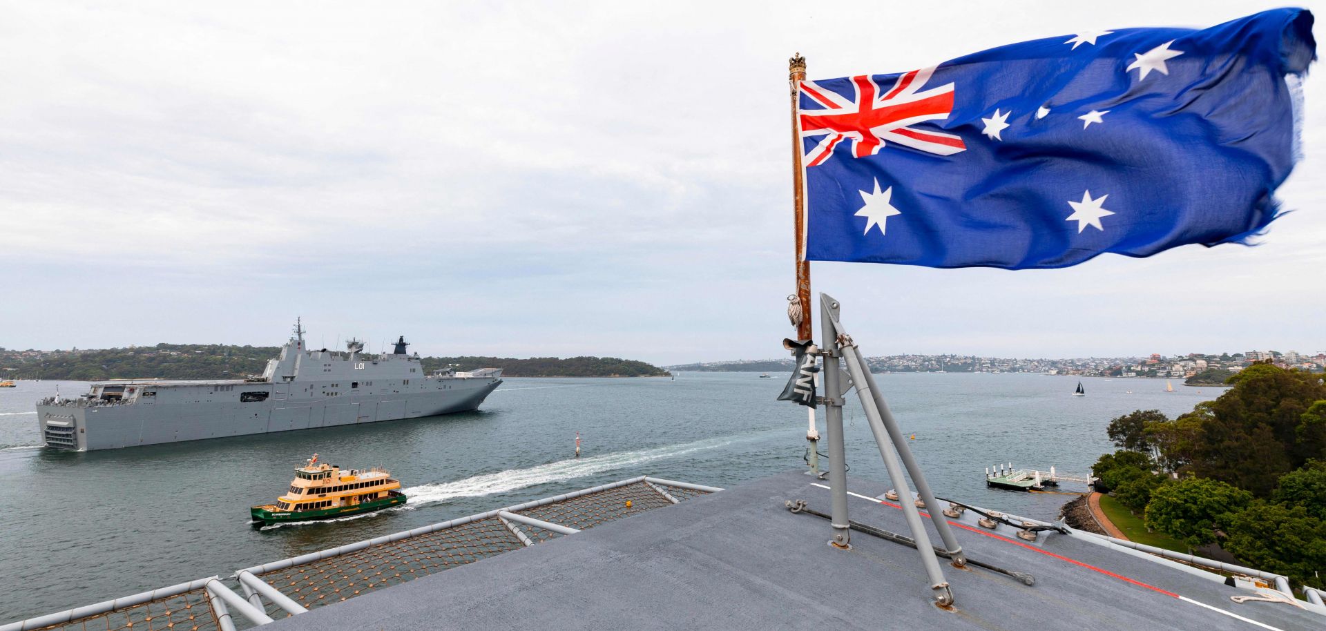 An Australian flag waves as a warship transits a waterway in the background in a photo taken on Jan. 18, 2020. 