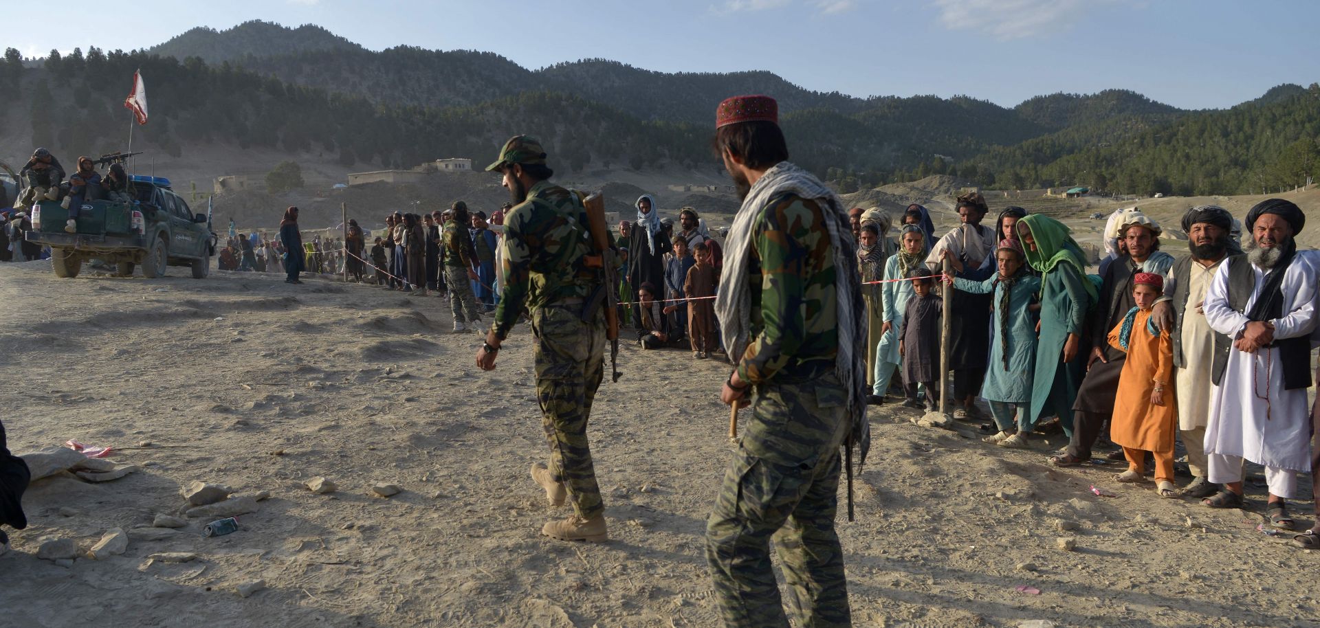 Taliban fighters stand guard on June 26, 2022, as people wait to receive aid in a village in Afghanistan’s Khost province after a recent earthquake.