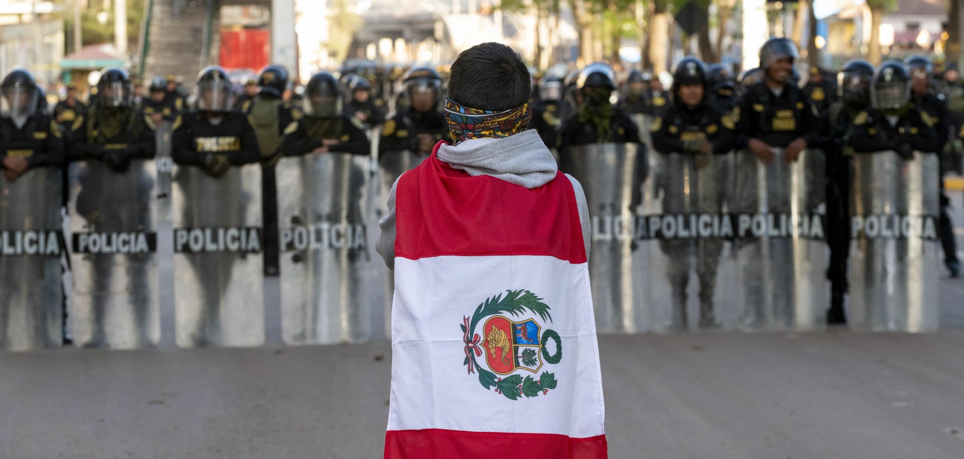 A demonstrator wearing the Peruvian flag stands in front of police officers forming a barrier with their riot shields near the entrance of the airport in Cusco, Peru, on Jan. 19, 2023.
