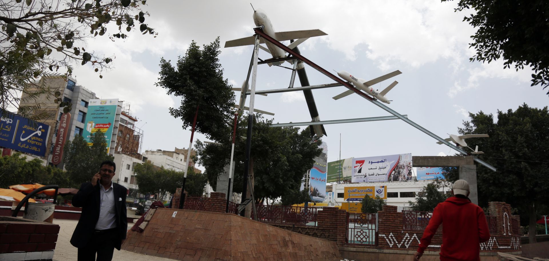 A photo taken in Sanaa, Yemen, on March 21, 2022, shows people walking under mock drones and missiles set up by supporters of the country's Iran-aligned Houthi movement, which earlier conducted attacks against Saudi energy facilities.