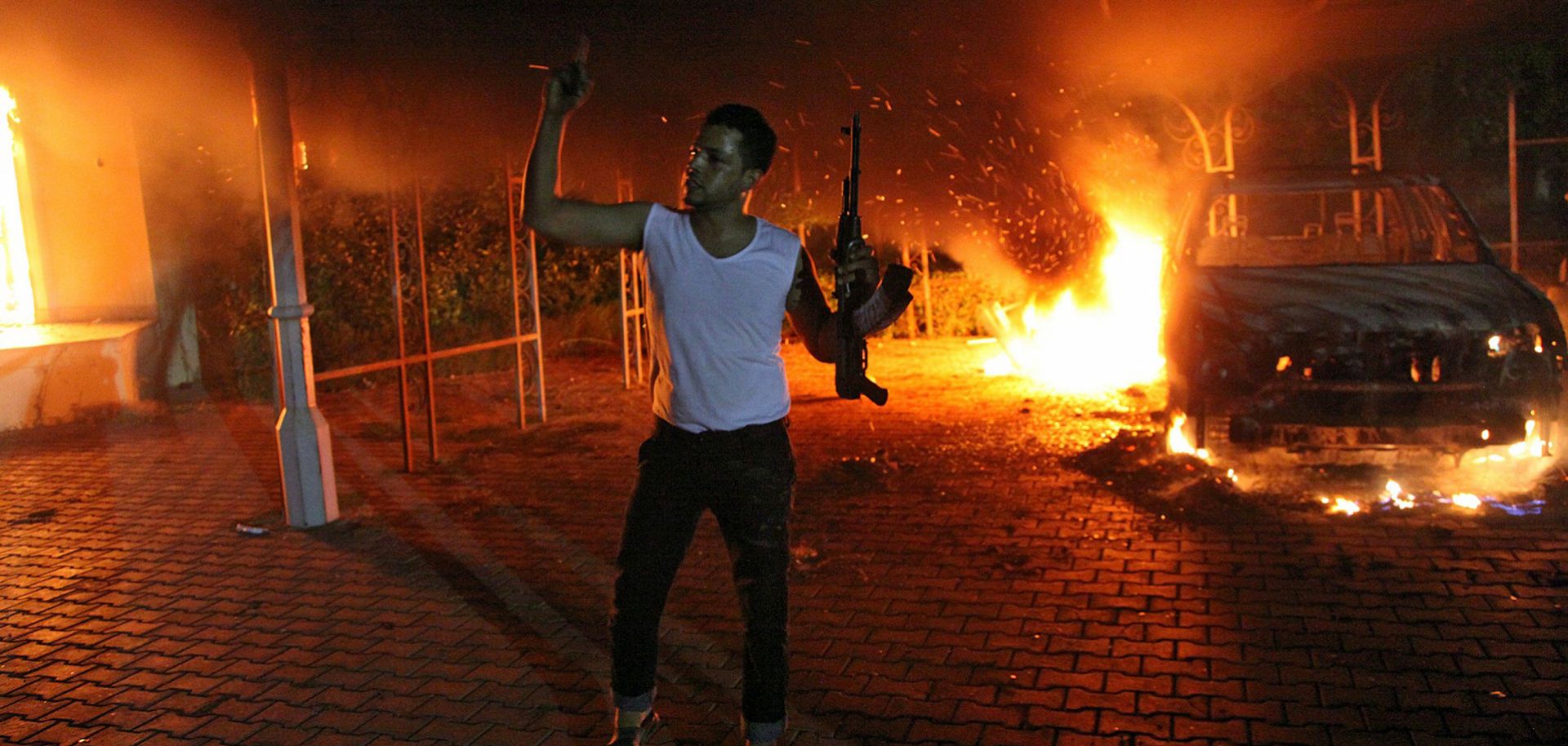 An armed man waves his rifle as buildings and cars are engulfed in flames after being set on fire inside the US consulate compound in Benghazi late on September 11, 2012.