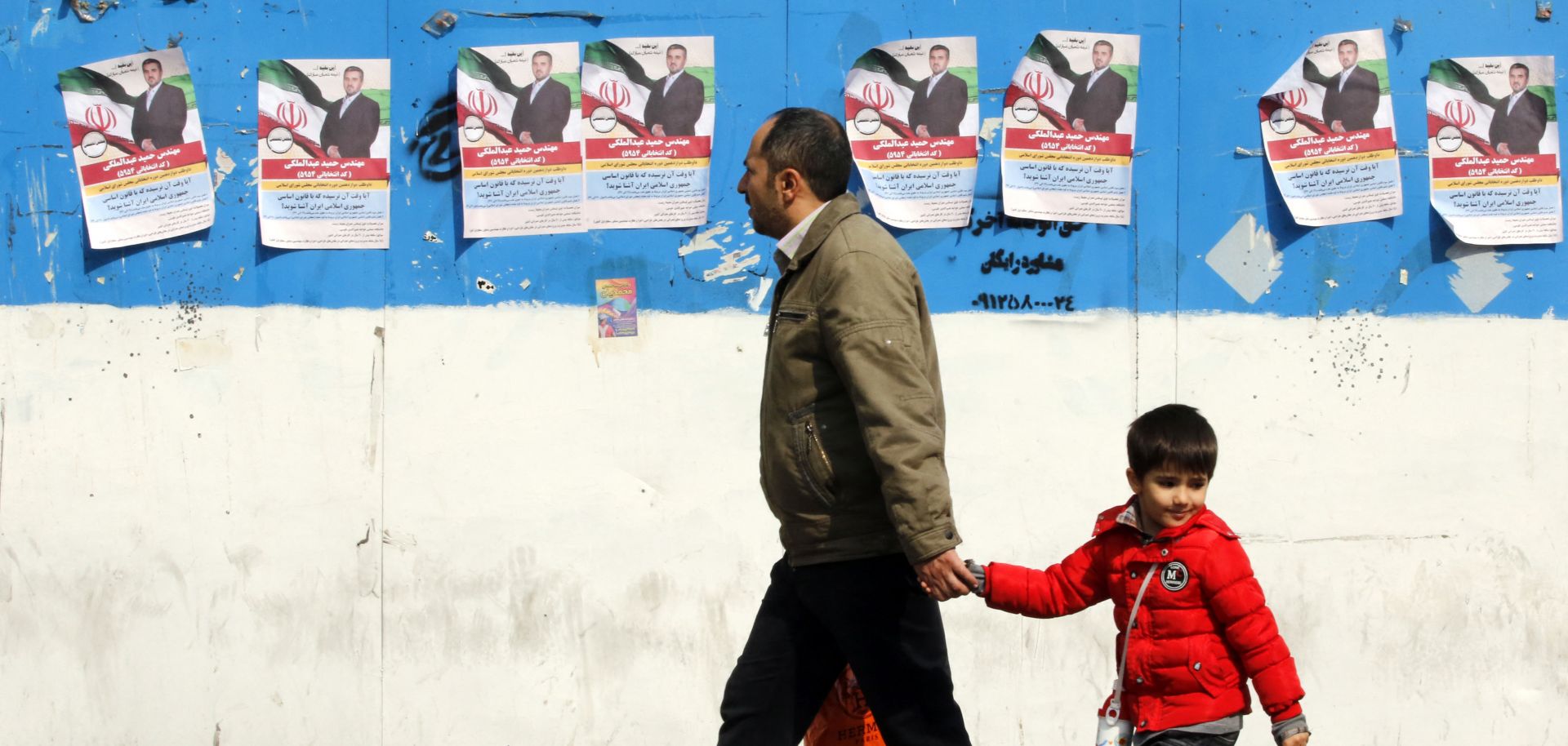 A man and a child walk past electoral campaign posters in Tehran, Iran, on Feb. 22, 2024, ahead of next month's elections.