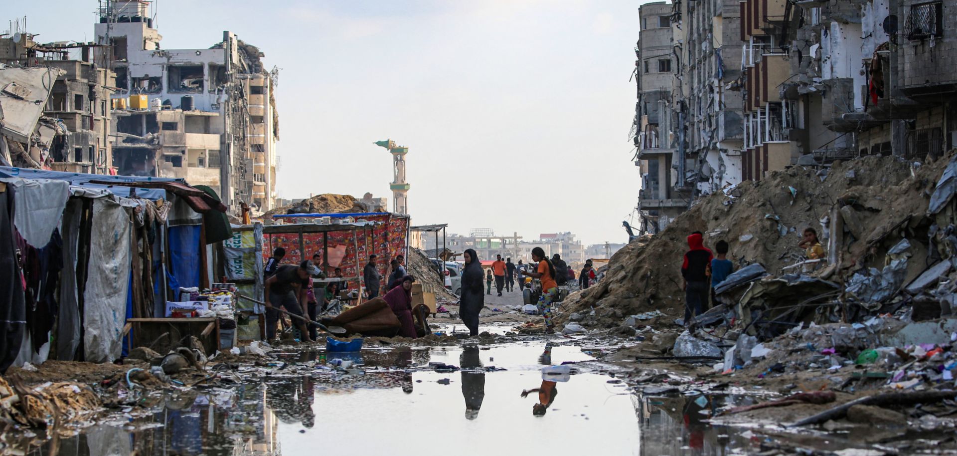 Displaced Palestinians walk around a puddle in front of destroyed buildings and tents in Khan Yunis in the southern Gaza Strip on May 16, 2024.