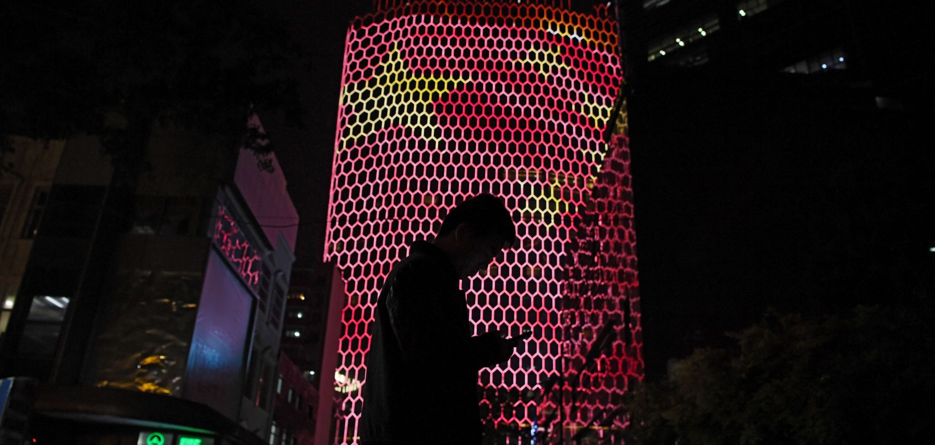 A man looks at his phone near a building in Beijing with a giant projected image of the Chinese national flag.