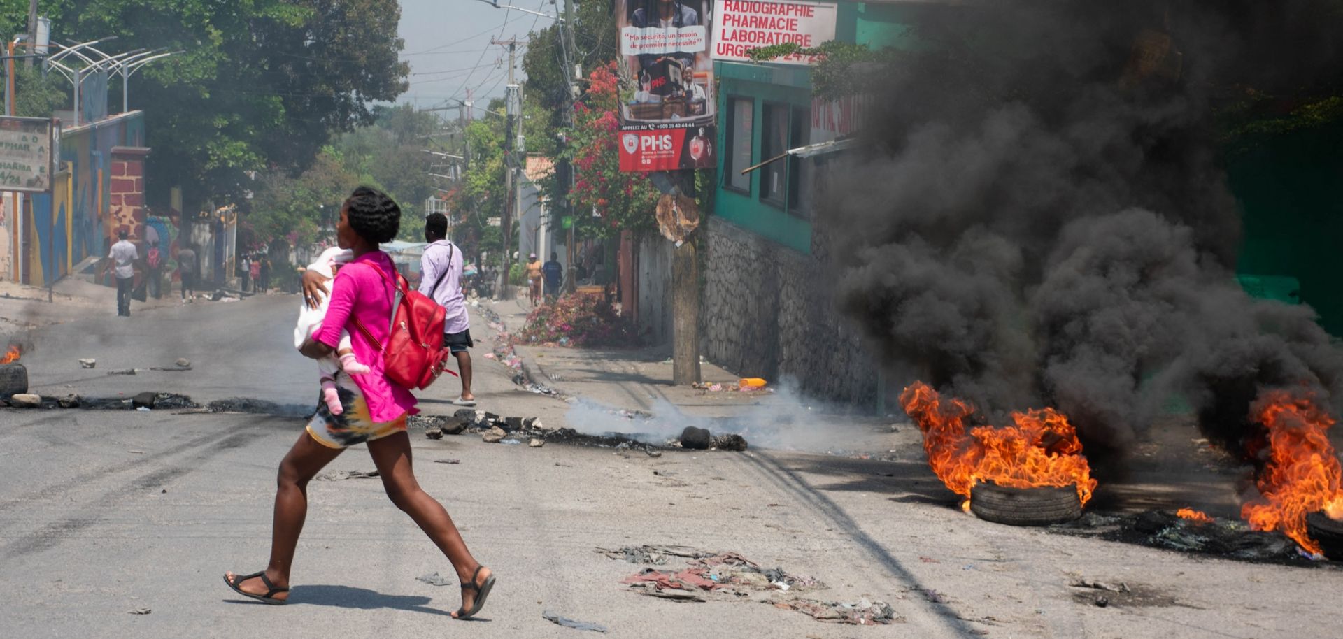 A woman carrying a child runs from an area in Port-au-Prince, Haiti, after hearing gunshots on March 20, 2024.