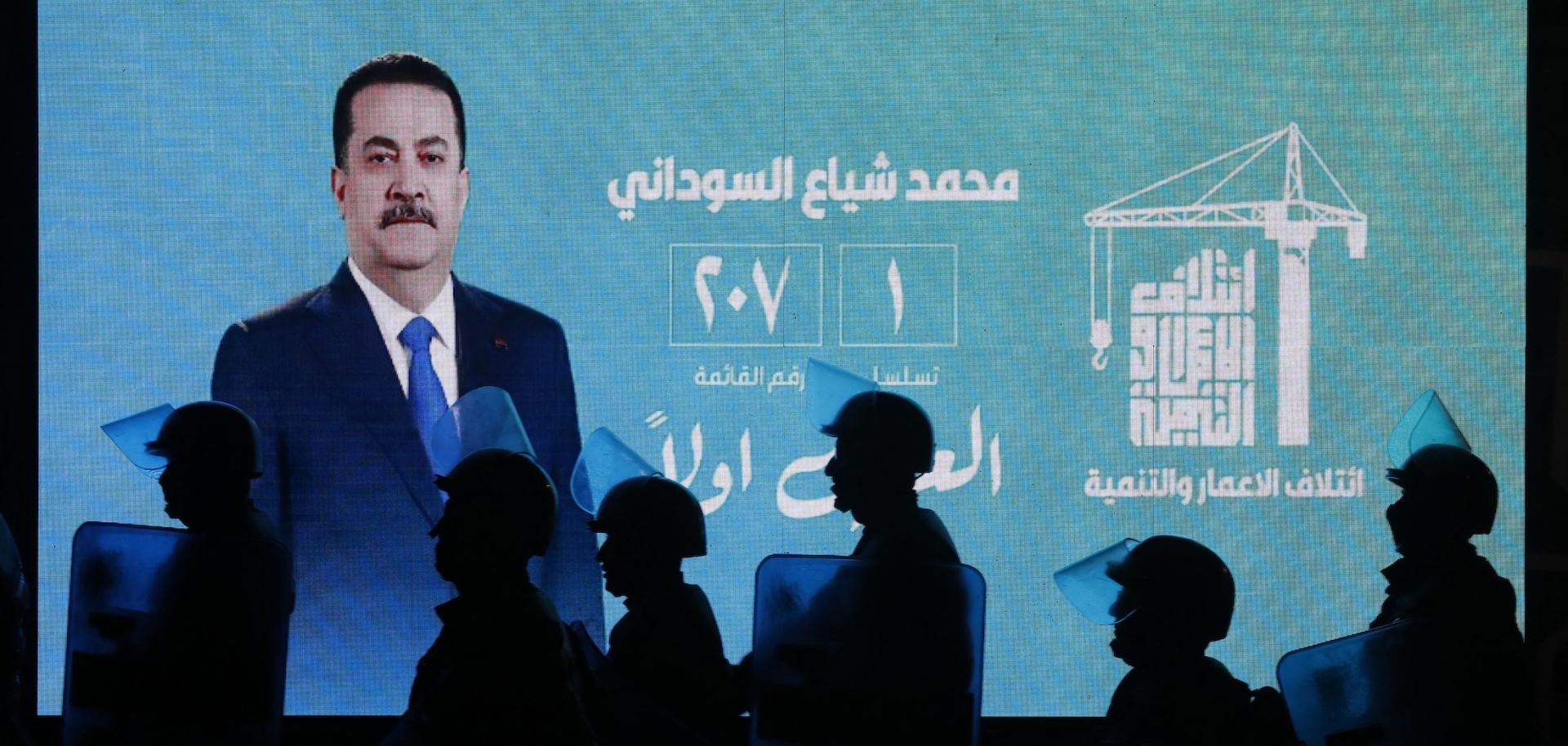 Iraqi riot police walk past a screen displaying a portrait of incumbent Iraqi Prime Minister Mohammed Shia al-Sudani during celebrations by his supporters following the announcement of preliminary election results in Baghdad on Nov. 12, 2025. 