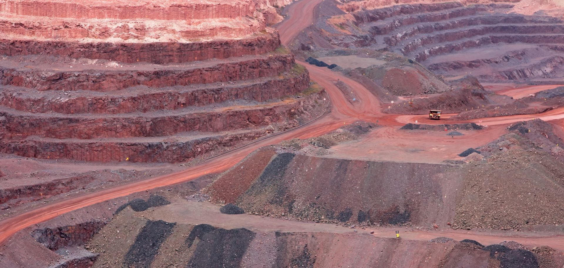 A stock photo shows a large, open-pit iron ore mine with various layers of soil.