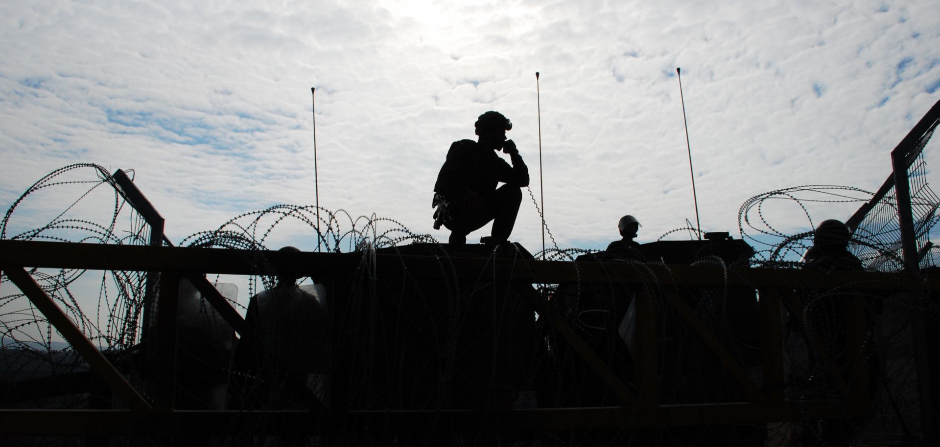 Israeli soldiers guard a barrier, silhouetted against afternoon sun.