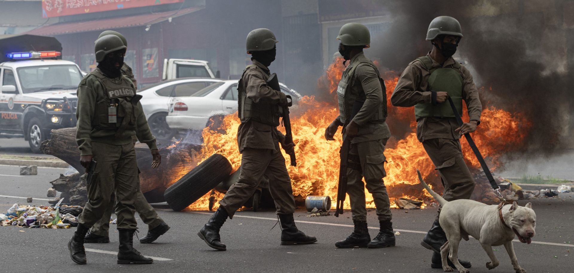 Anti-riot police officers with dogs walk past burning barricades made by protesters in Maputo, Mozambique, on Nov. 7, 2024. 