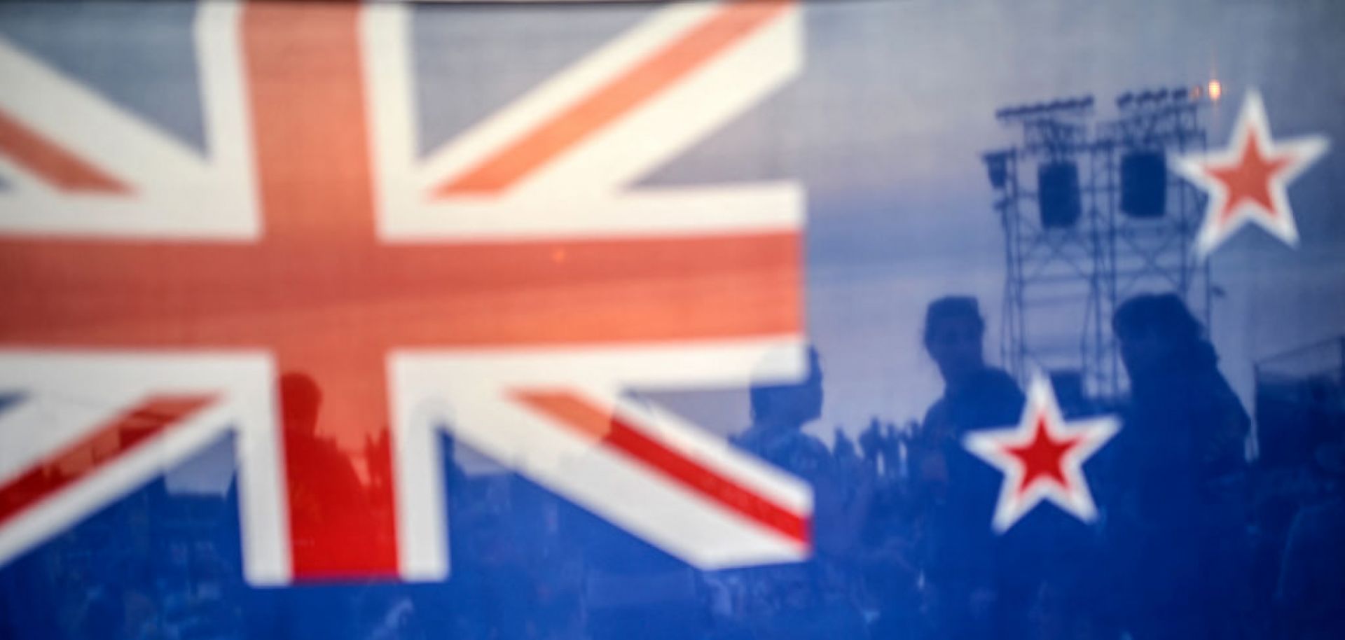 People are seen behind a New Zealand flag during a ceremony celebrating the anniversary of Anzac Day. 