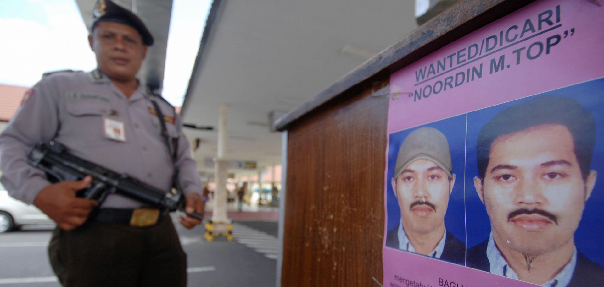 A policeman next to a poster of Noordin Mohammed Top on Aug. 8, 2009, at Bali's Denpasar airport.