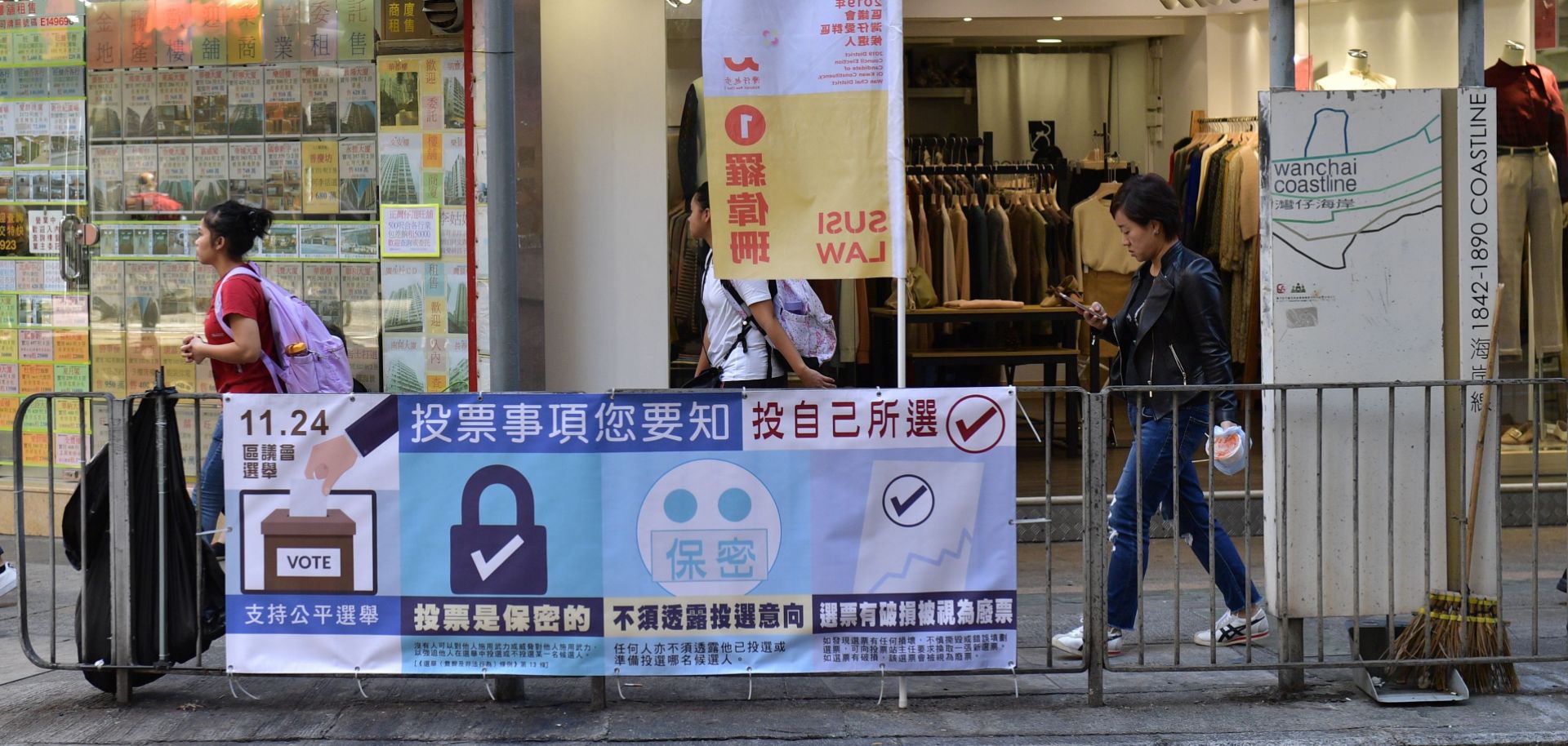 This Nov. 22, 2019, photo shows pedestrians walking past a banner for Hong Kong's district council elections, which are scheduled to take place Nov. 24.