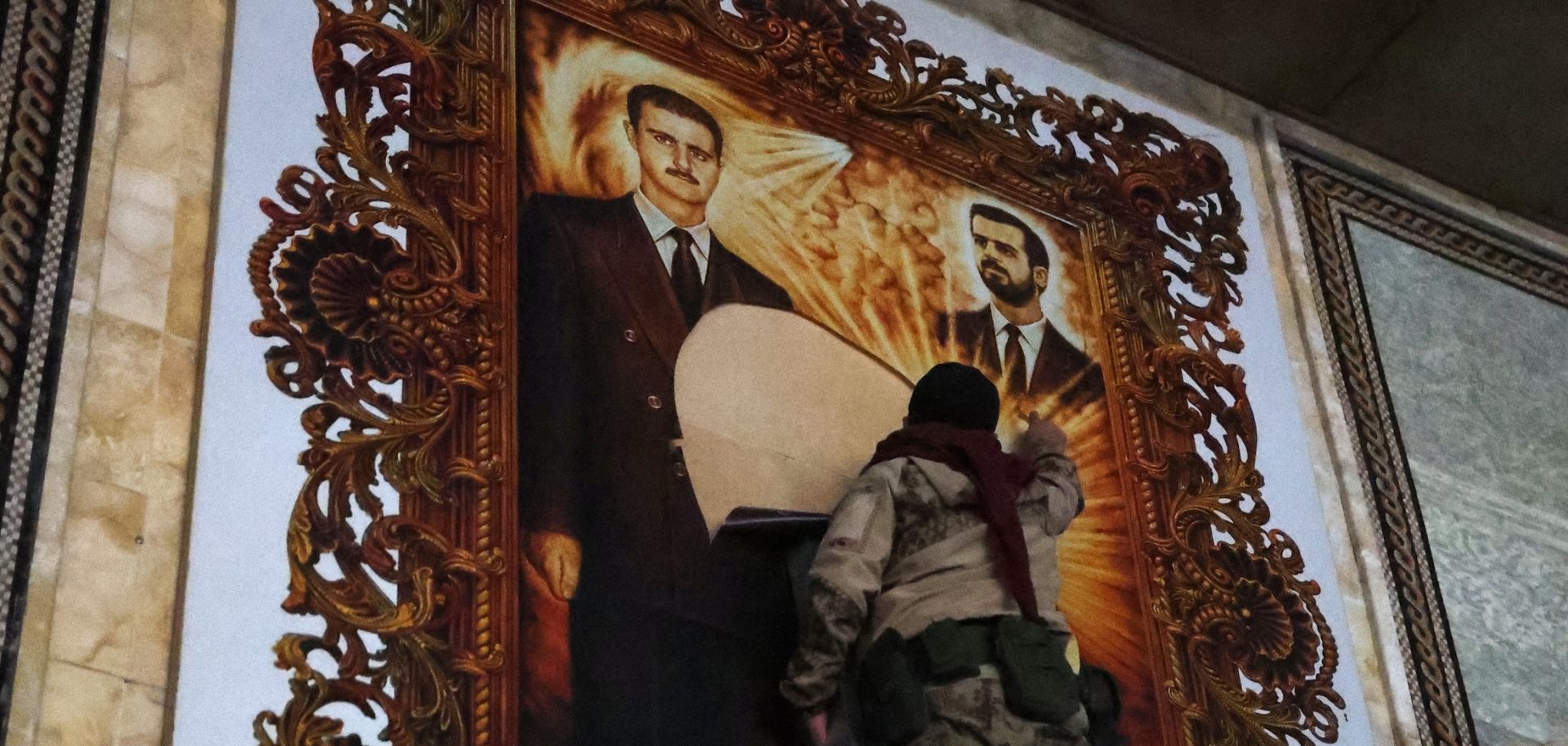 An anti-regime fighter tears off a poster depicting Syrian President Bashar al Assad (left) and his brother Maher at the airport in the northern Syrian city of Aleppo on Dec. 2, 2024. 