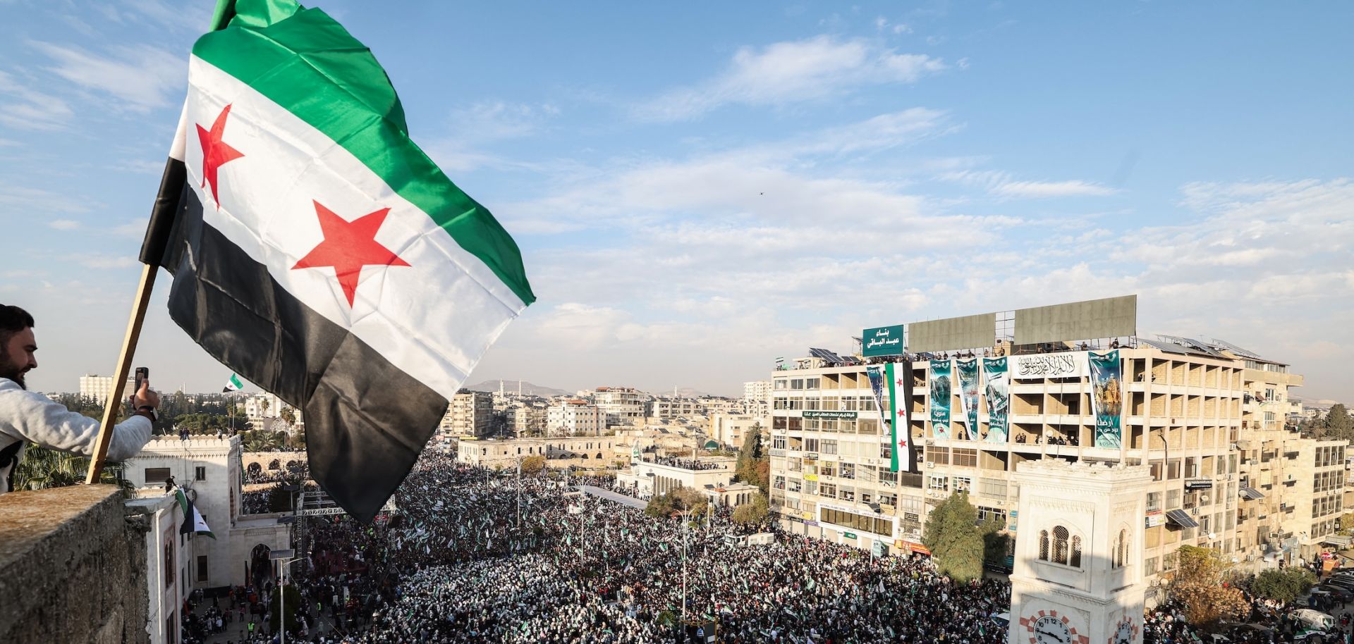 A Syrian flag flutters above crowds gathering in central Hama, Syria, during celebrations on Dec. 5, 2025, marking one year since the fall of former President Bashar al Assad's regime.
