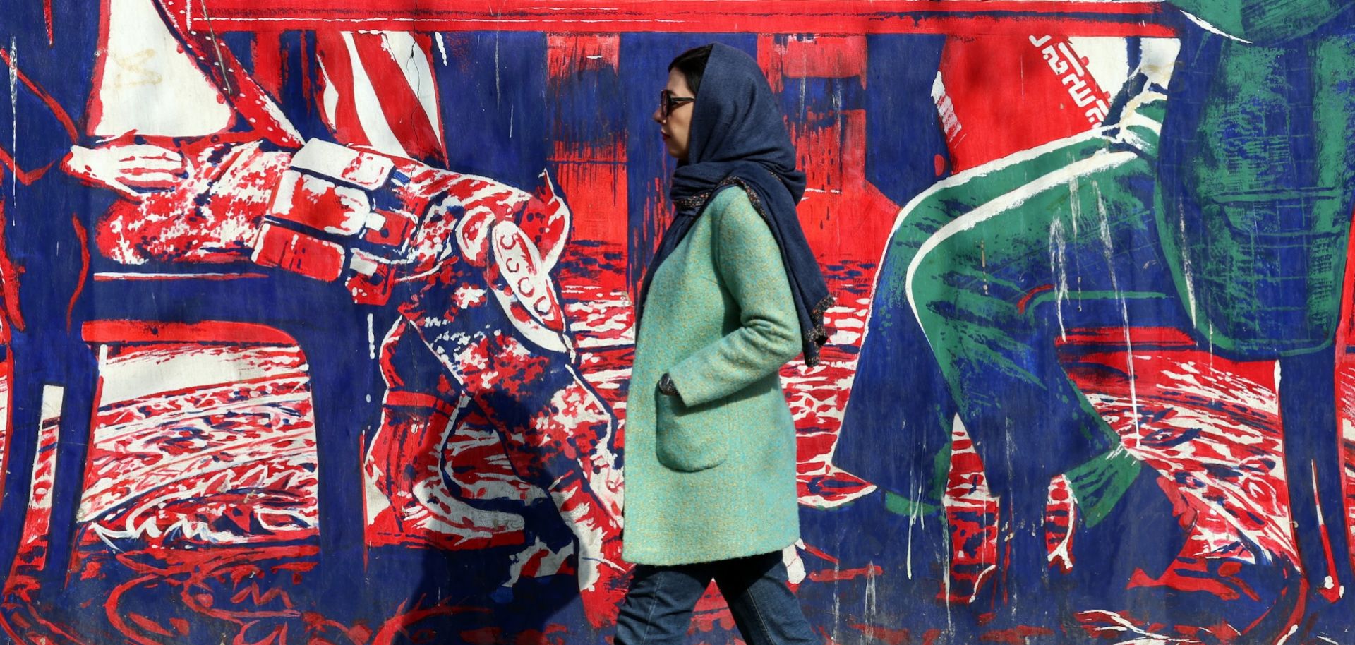 An Iranian woman walks past a mural depicting Iran and the United States at the negotiation table, painted on the outer walls of the former U.S. embassy in Tehran, on Feb. 6, 2026.