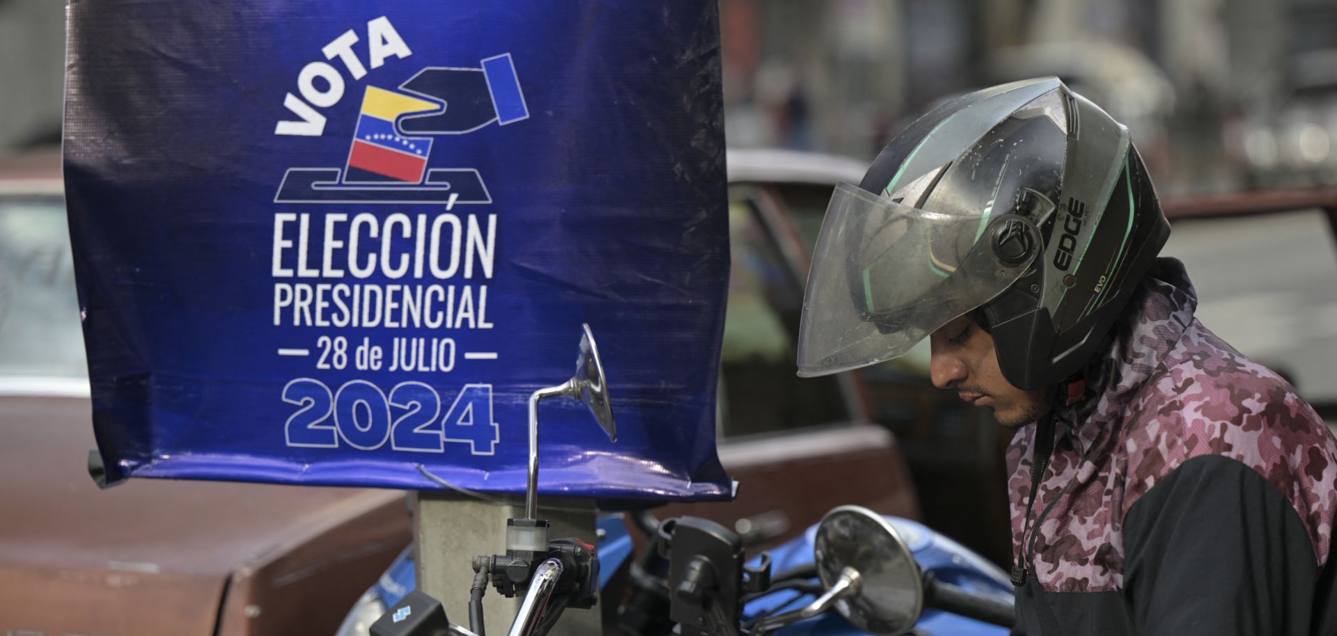 A motorcyclist looks at his phone in front of a National Electoral Council poster promoting the upcoming presidential election in Caracas, Venezuela, on July 23, 2024.