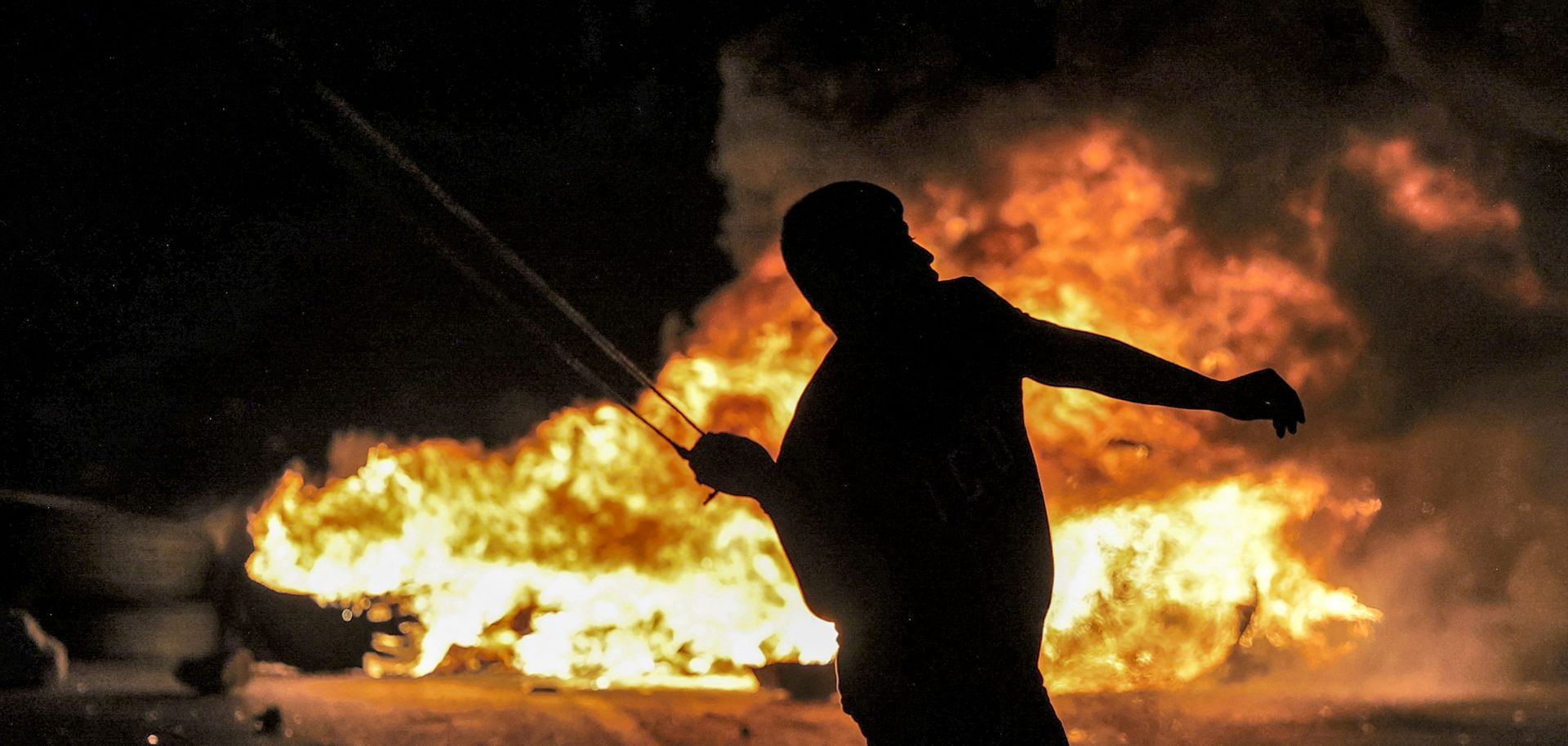 A Palestinian youth throws a rock with a slingshot at Israeli security forces during Oct. 3, 2022, clashes at the northern entrance of the city of Ramallah in the West Bank.