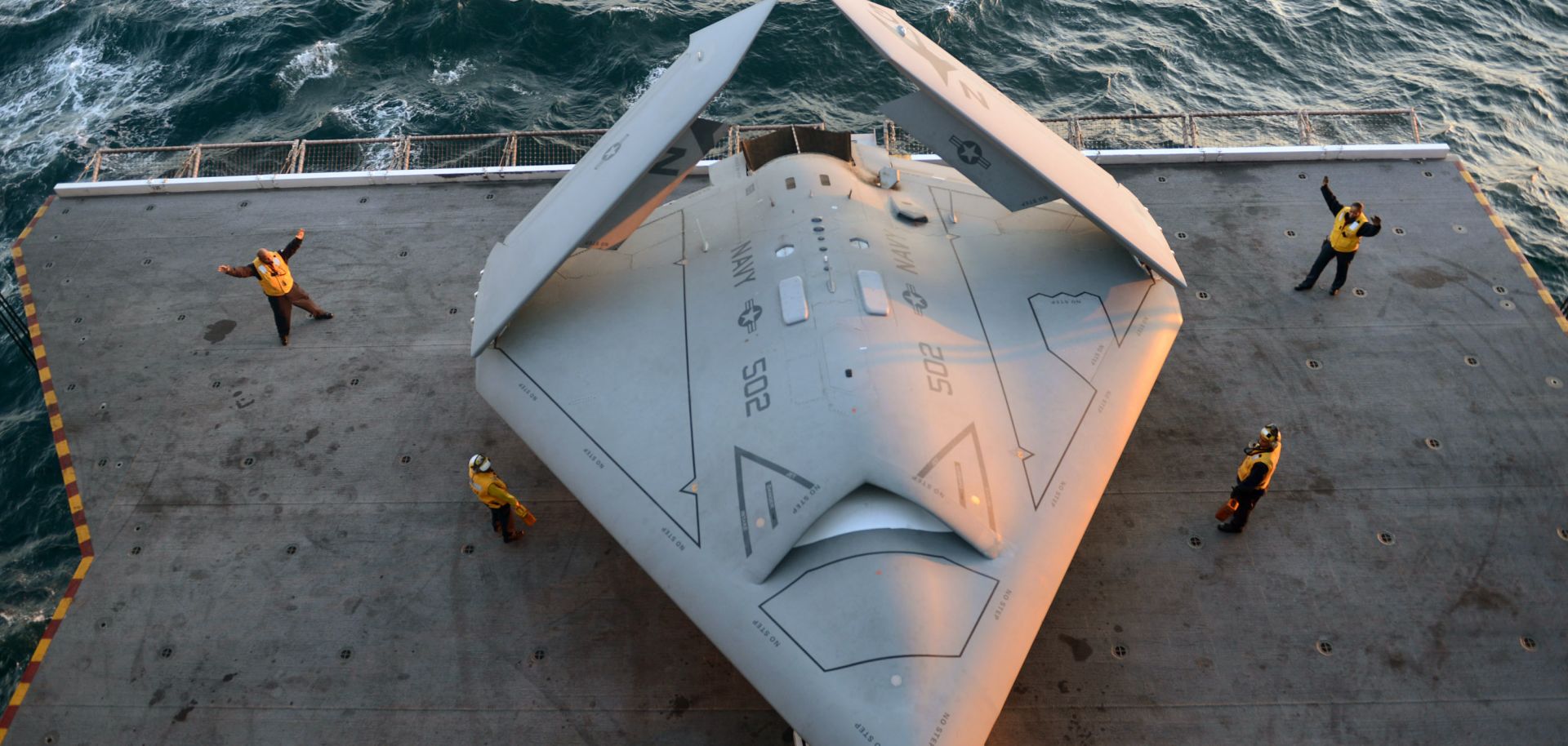 A picture showing U.S. sailors move an X-47B Unmanned Combat Air System (UCAS) demonstrator onto an aircraft elevator aboard the aircraft carrier USS George H.W. Bush.