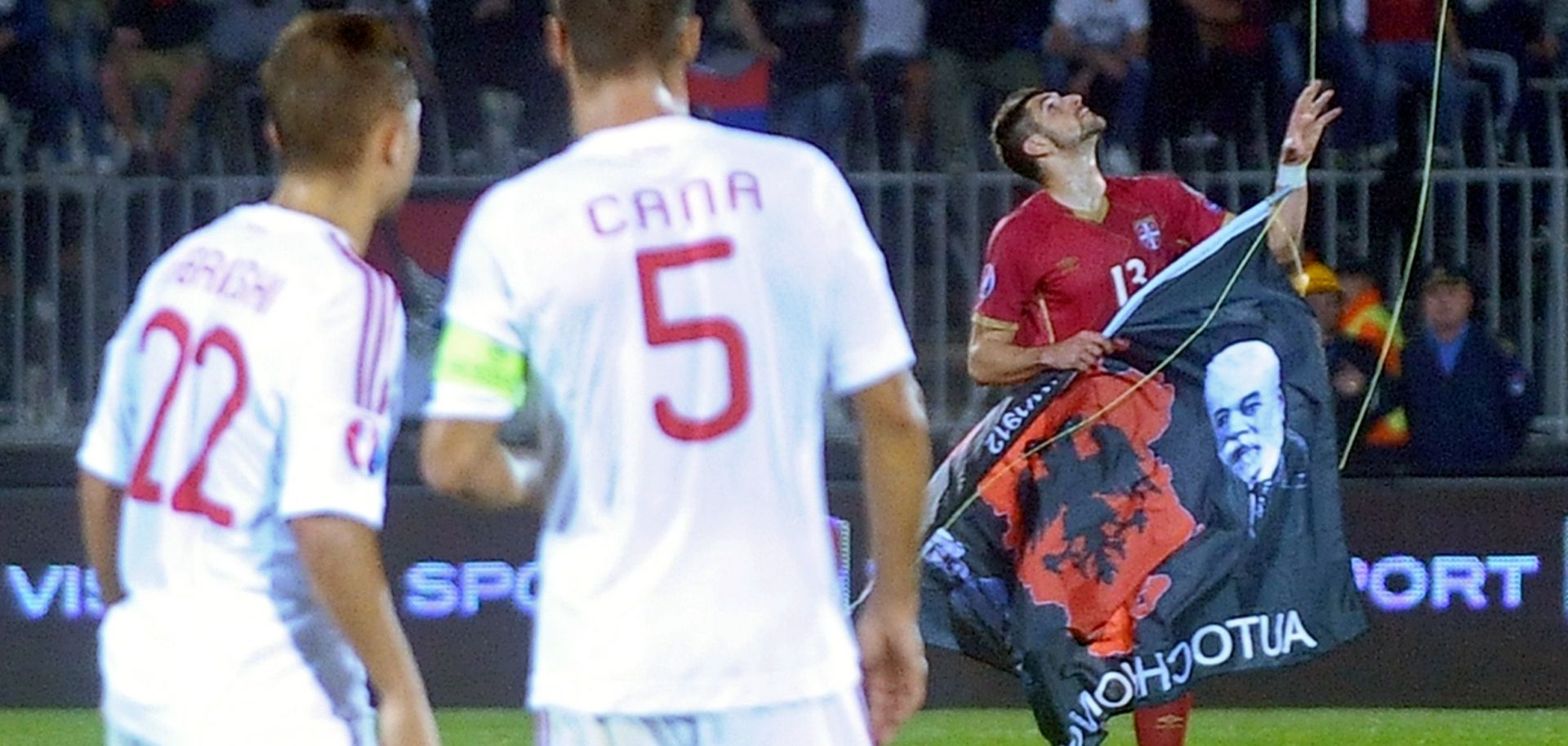 Albania's players look as Serbian soccer player grabs a flag with Albanian national symbols.