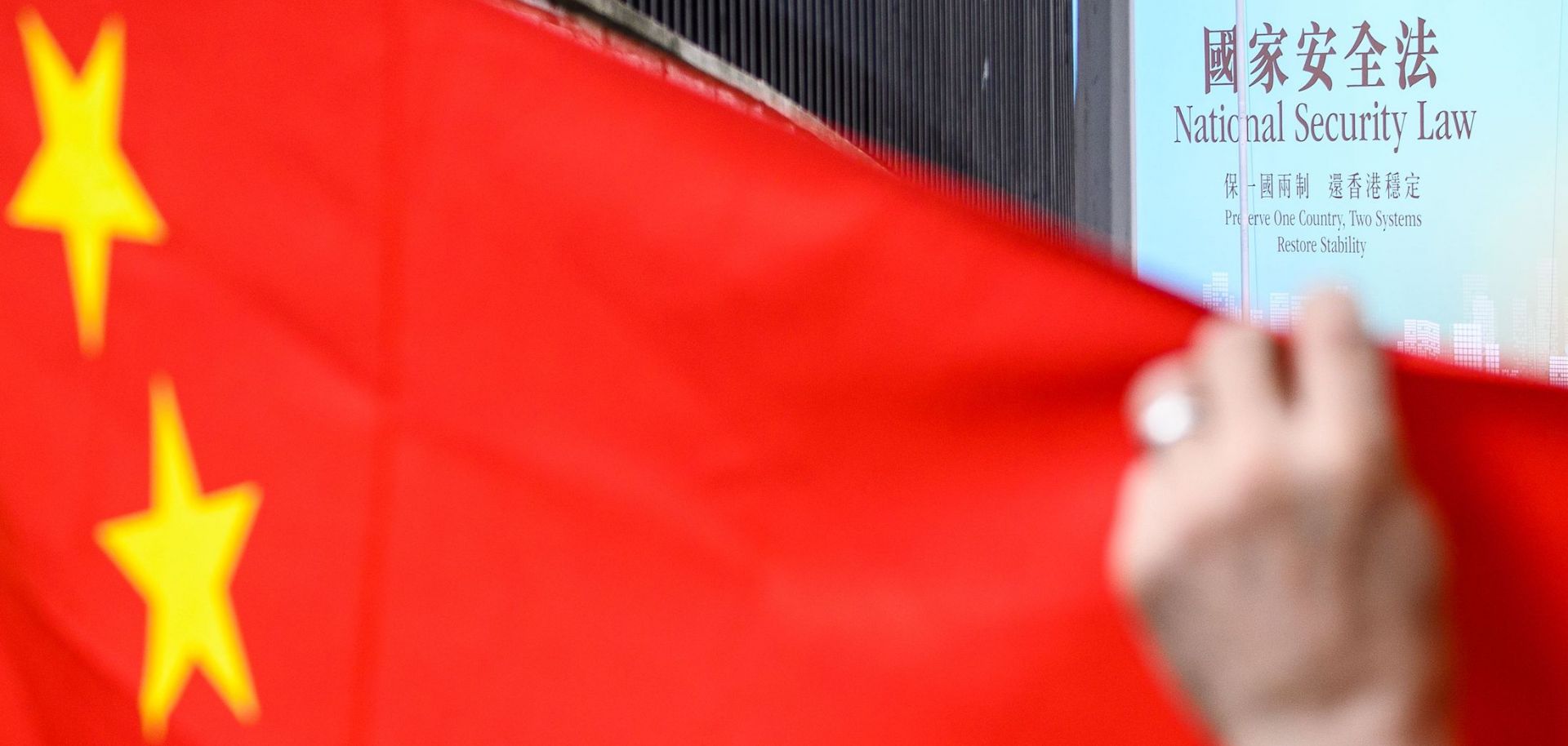 A billboard (top R) referring to the incoming National Security Law is seen beyond a Chinese national flag being held up by a pro-China activist during a rally outside the US Consulate General in Hong Kong