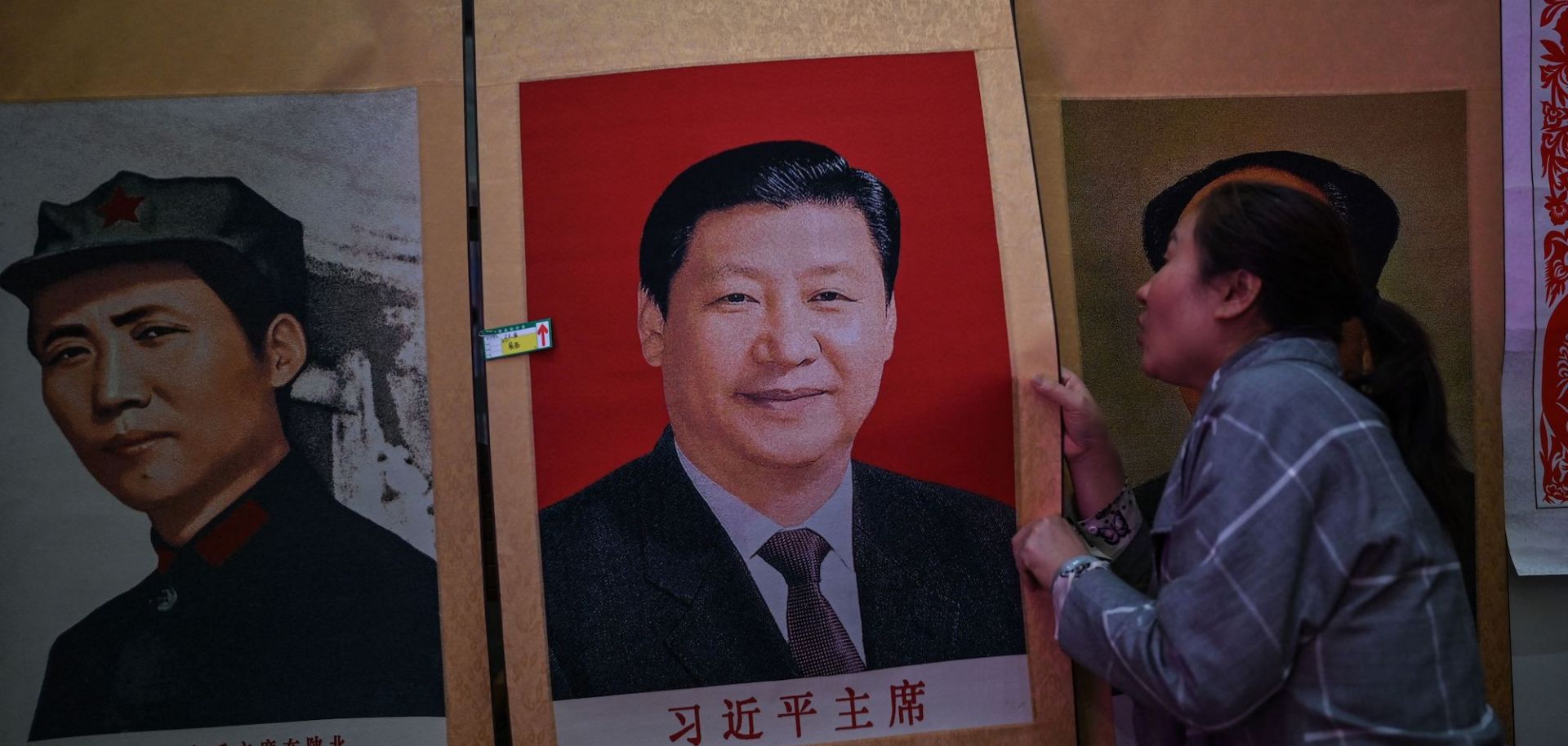 This picture taken during a government organised media tour shows a seller holding a portrait of the Chinese President Xi Jinping next to a picture of the former Chinese leader Mao Zedong at Dongfanghong Theatre in Yan'an, the headquarters of the Chinese Communist Party from 1936 to 1947, in Shaanxi province on May 10, 2021, ahead of the 100th year of the party's founding in July. 