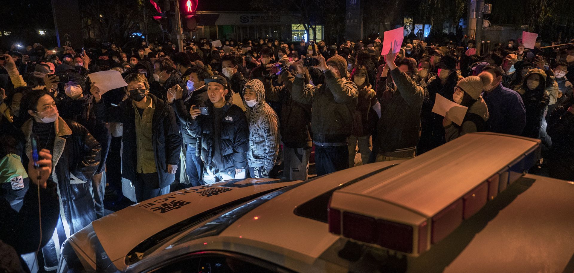 Protesters march by a police cruiser during a protest against China's strict "zero-COVID" measures on Nov. 27, 2022, in Beijing.