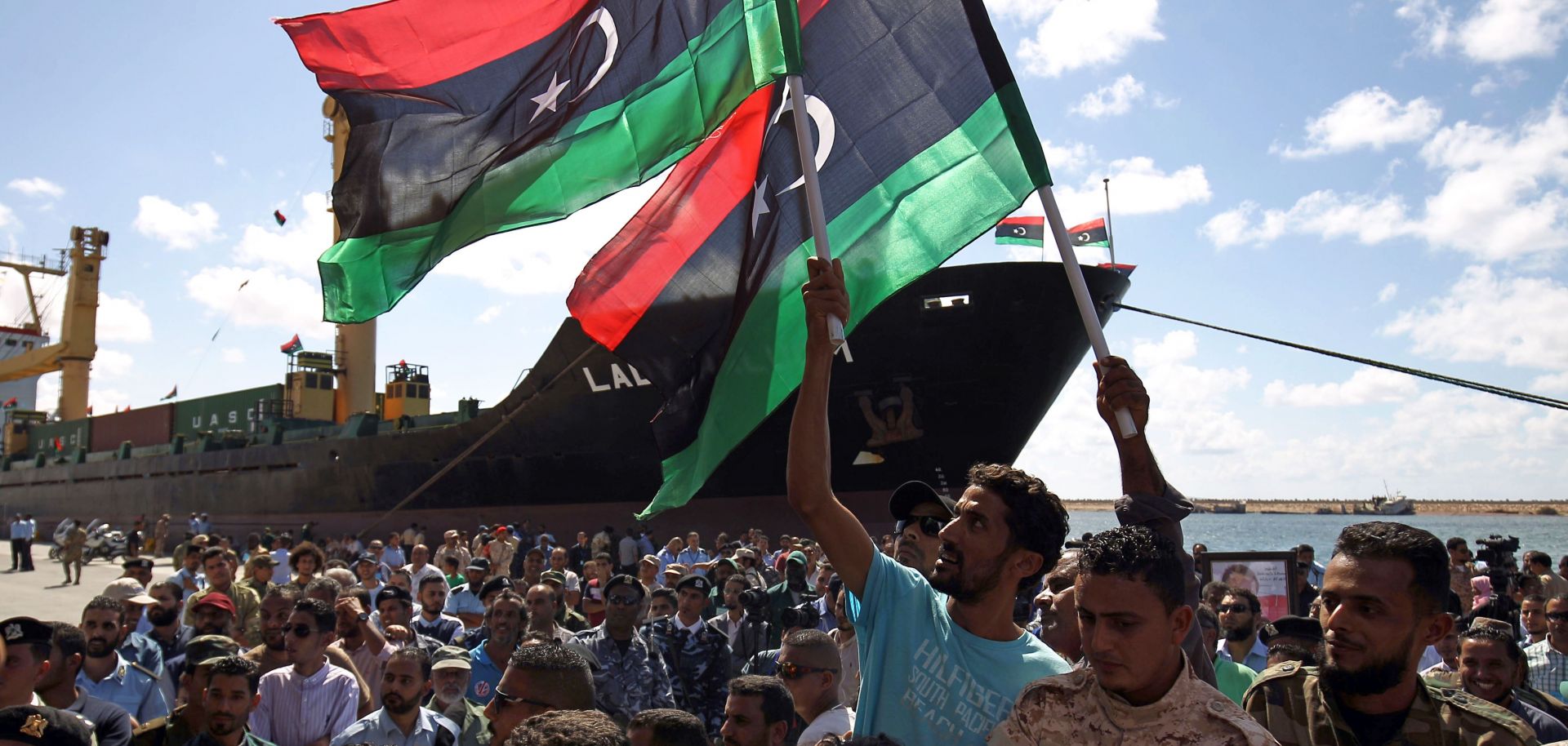 In this photograph, Libyans wave their national flag at the port of Benghazi during a ceremony marking its reopening in October 2017.
