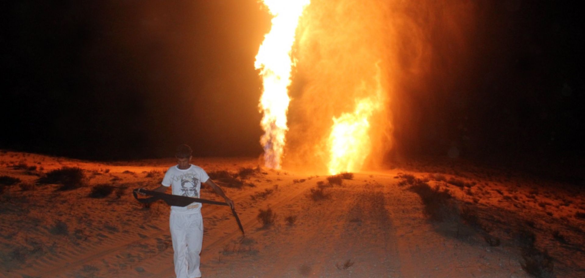 An Egyptian man walks in front of an enormous flame by a gas pipeline.