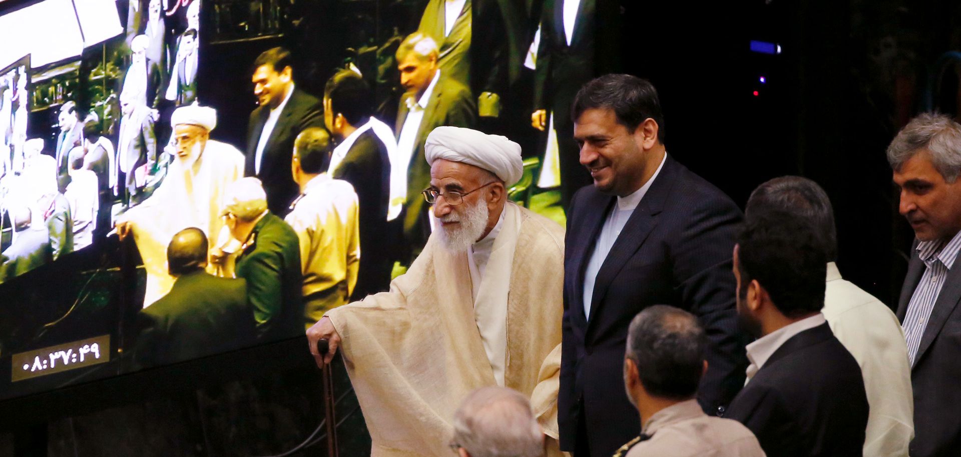 The head of Iran's Assembly of Experts walks past a TV screen at the opening session of the Majlis in Tehran. The assembly is preparing to weigh in on who should compete for the country's highest elected office.