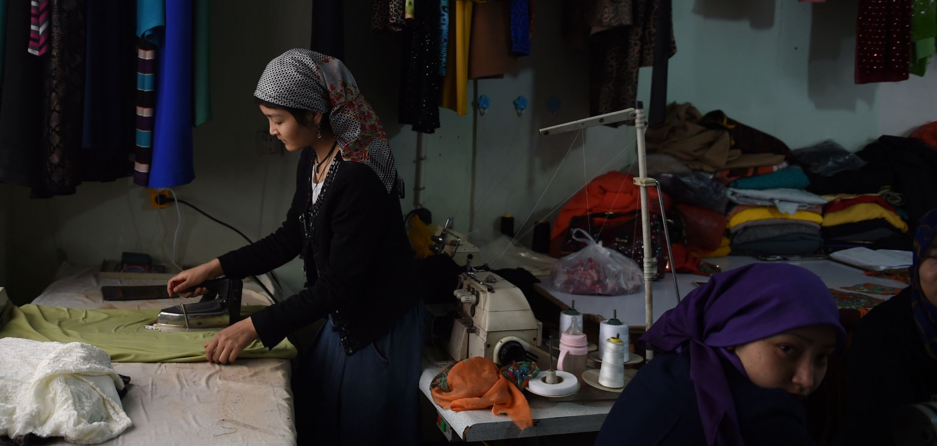 young girls ironing and sewing clothes in a workshop above a bazaar.