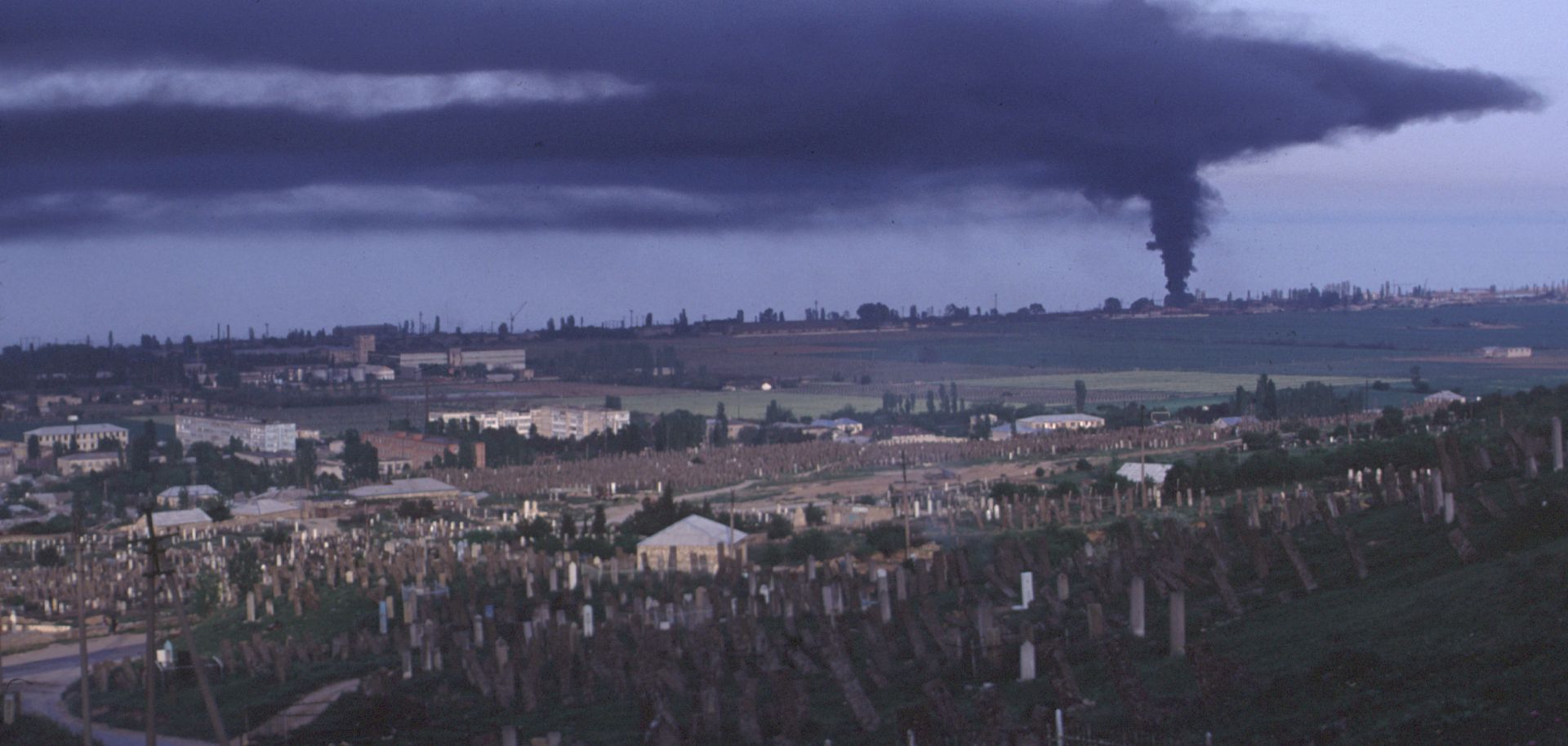 View of the town and an historic Ottoman Empire cemetery as plumes of black smoke pours from a tire factory.