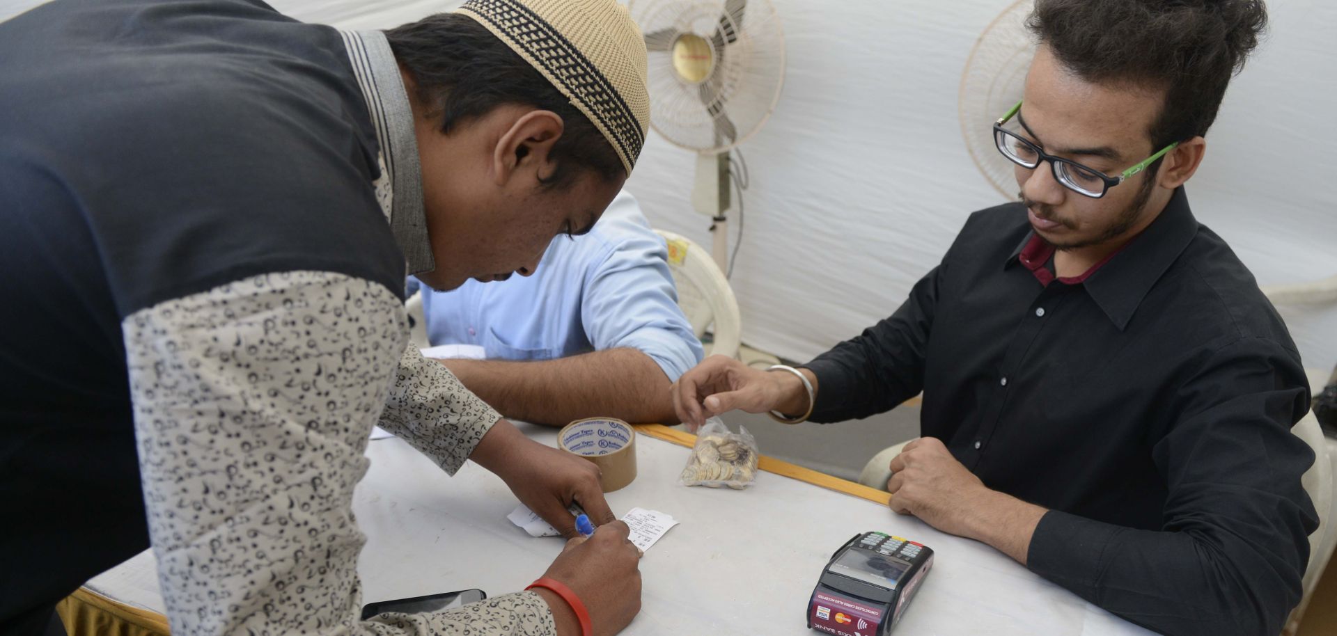 An Indian man signs his name to use a makeshift ATM as a bank cashier looks on in December 2016.