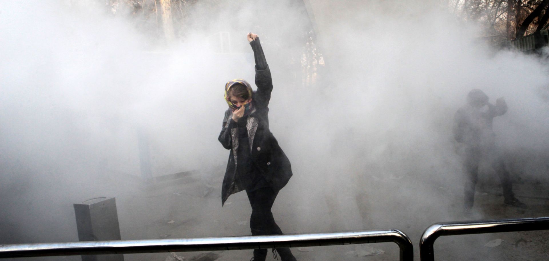 An Iranian woman raises her fist amid the smoke of tear gas at the University of Tehran during a protest in the capital, Tehran, on Dec. 30, 2017.