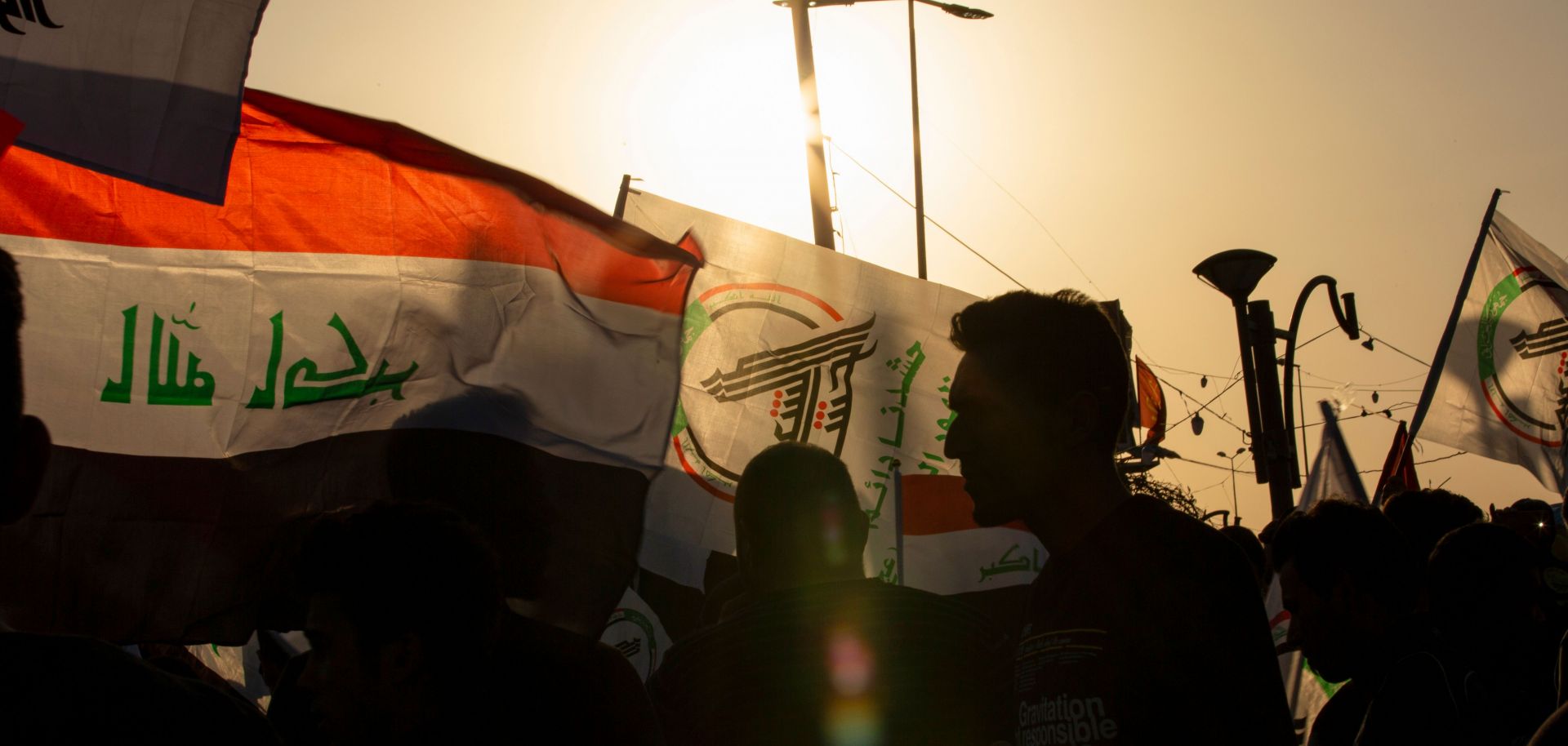 Protesters waving the Iraqi flag alongside one of an armed network march in Basra to denounce U.S. airstrikes that killed dozens of Iraqi militia members.