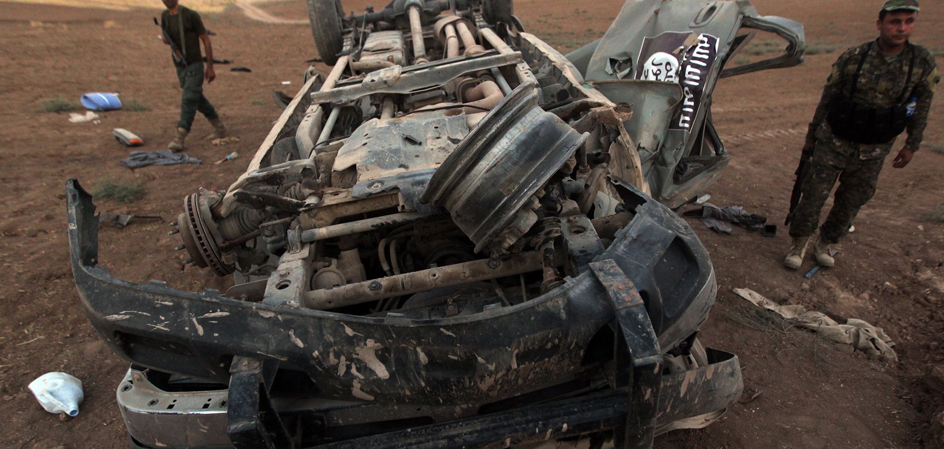 Peshmerga fighters inspect the remains of a car, bearing an image of the trademark jihadist flag, which reportedly belonged to Islamic State (IS) militants after it was targeted by an American air strike in the village of Baqufa, north of Mosul, on August 18, 2014. Kurdish peshmerga fighters backed by federal forces and US warplanes pressed a counter-offensive Monday against jihadists after retaking Iraq's largest dam, as the United States and Britain stepped up their military involvement.