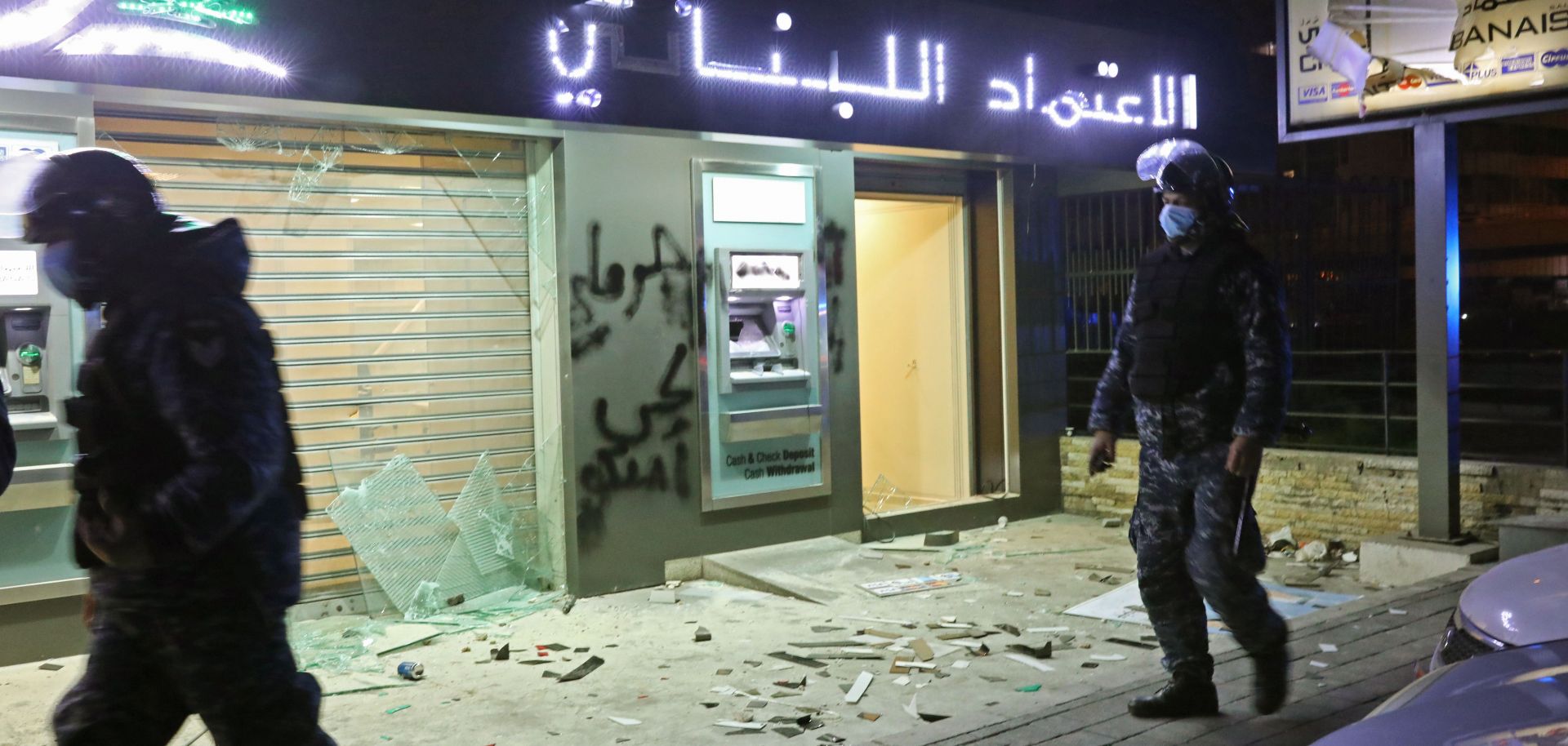 Lebanese police walk by a bank vandalized during protests in Beirut on Jan. 16, 2020.