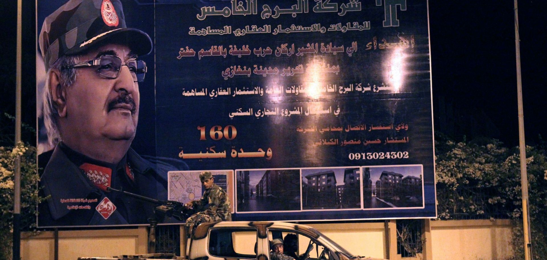 Members of the Libyan Special Forces, who are loyal to Khalifa Hifter, ride in a pickup truck past a billboard bearing the strongman's image in Benghazi during September 2017.