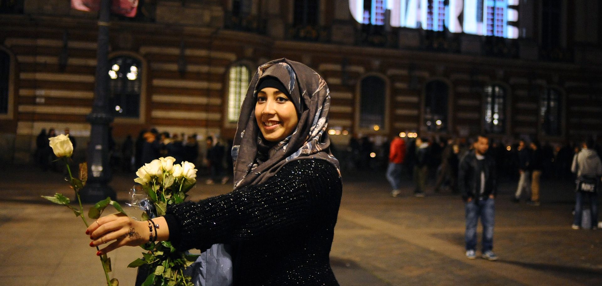 A woman holds a white rose near the Toulouse capital building in Jan. 2015 beneath a motto of solidarity for the victims of the Charlie Hebdo attacks.