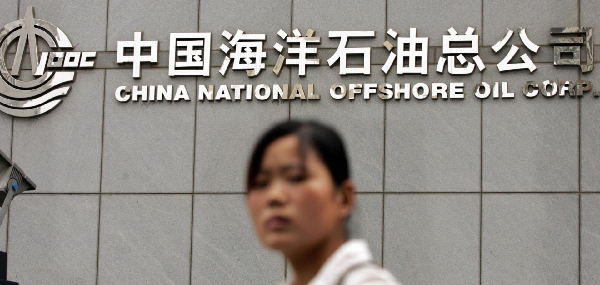 A woman walks past the headquarters of the state-run energy firm China National Offshore Oil Corp. in Beijing.