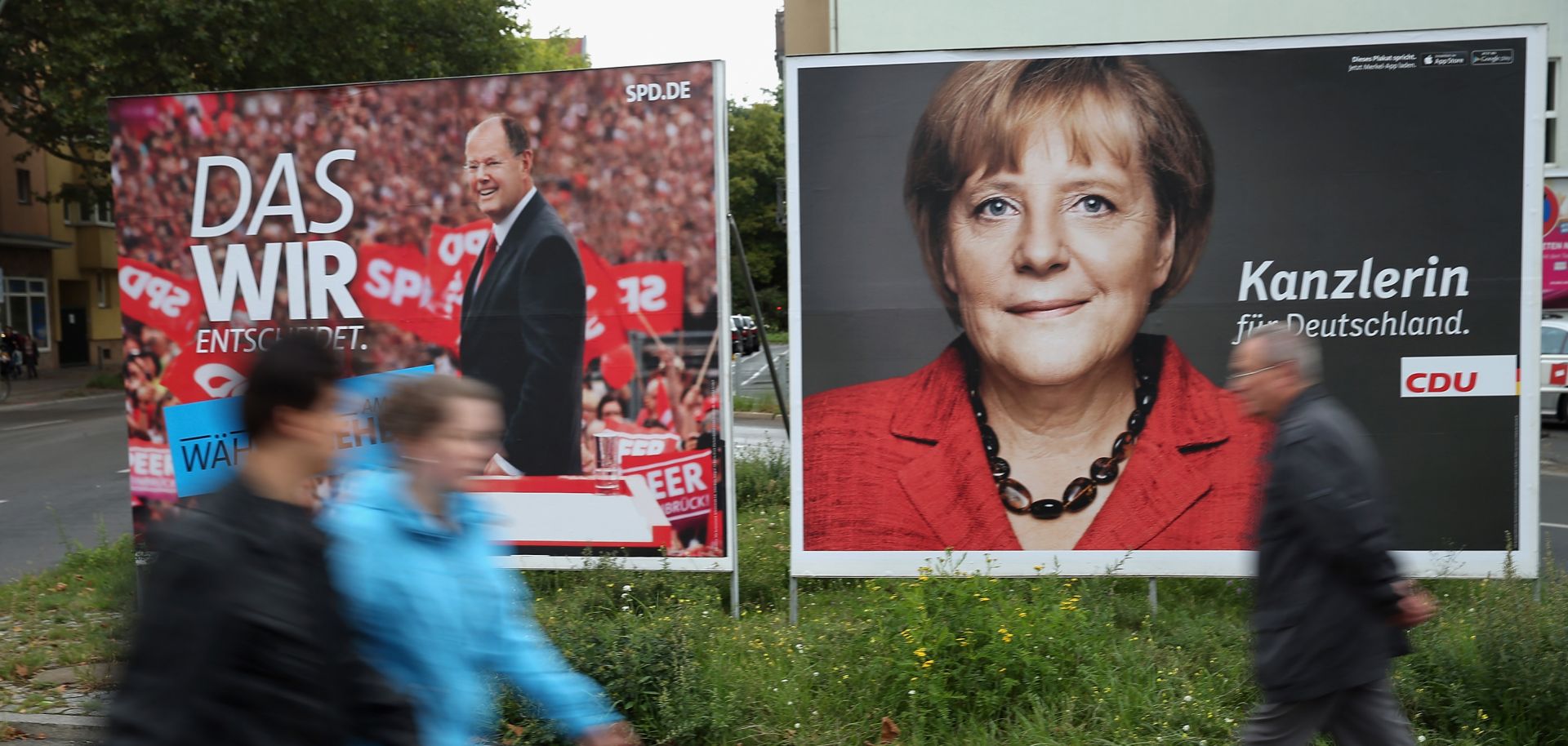 People walk past election campaign posters featuring Germany's Christian Democratic Union (CDU) Angela Merkel (R) and Social Democratic Party (SPD).