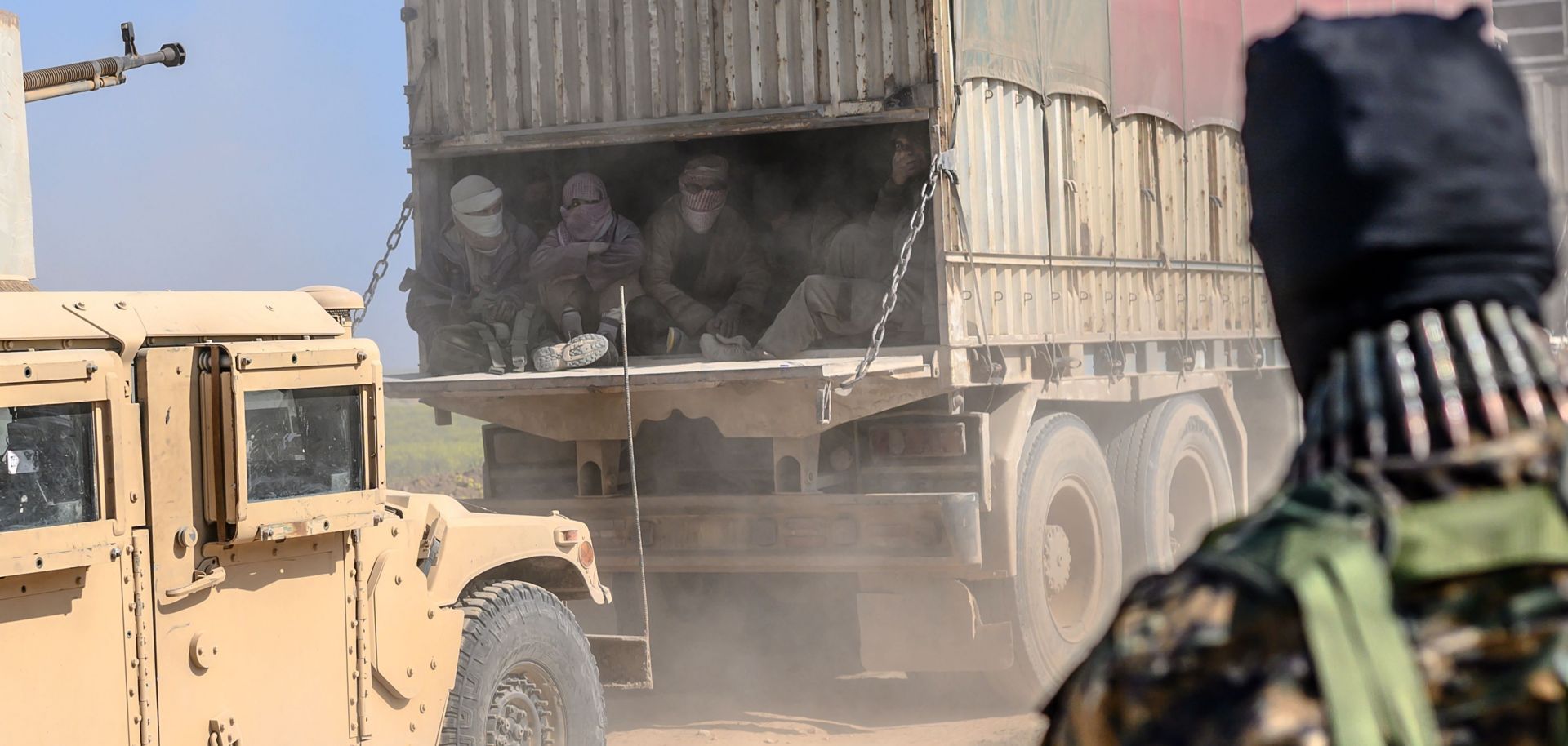 A truck carries men identified as Islamic State fighters on Feb. 20, 2019, near Baghouz, Syria. The fighters surrendered to Kurdish-led Syrian Democratic Forces.